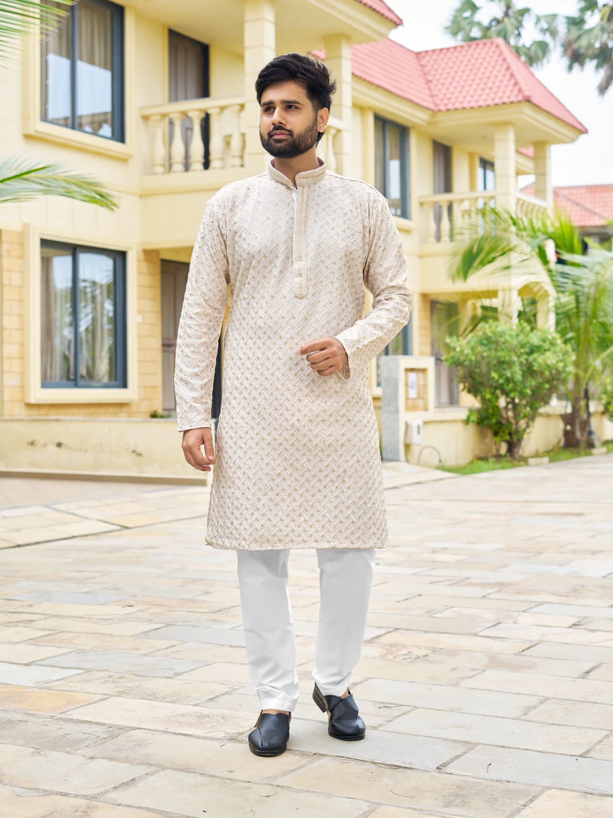 Man wearing a white traditional kurta in front of a house