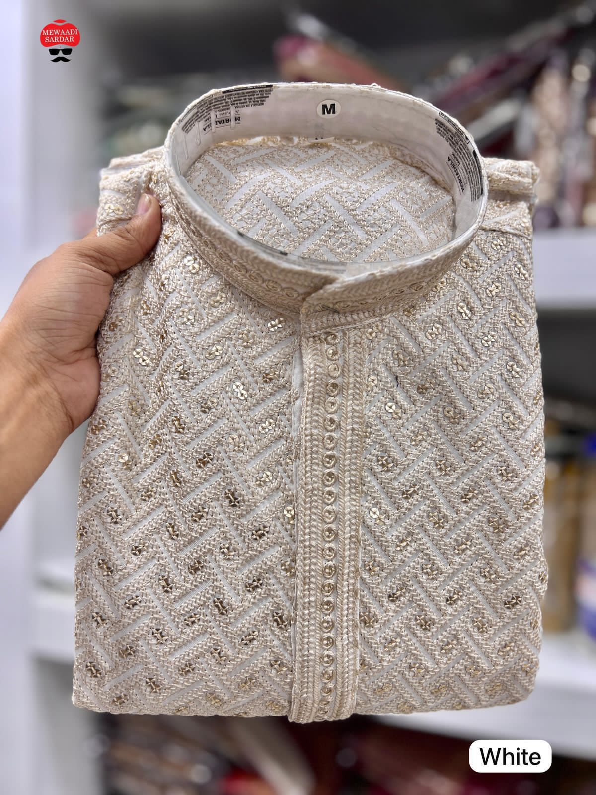 White embroidered jacket held by a hand with a blurred background