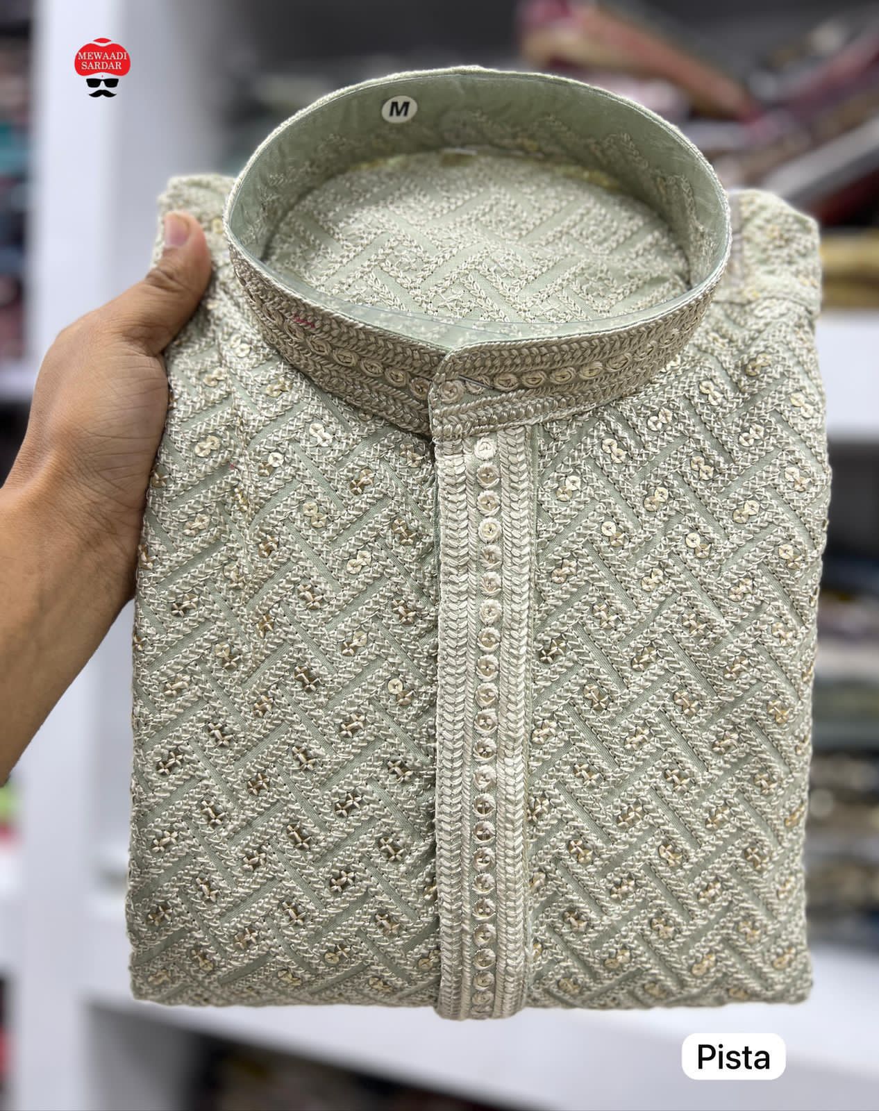 Pista traditional embroidered shirt held by a hand with a blurred background