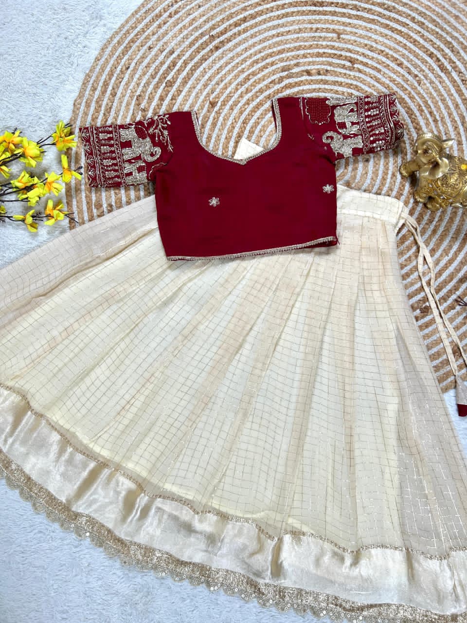 Red blouse with cream embroidery on a with gold border, placed on a textured surface.