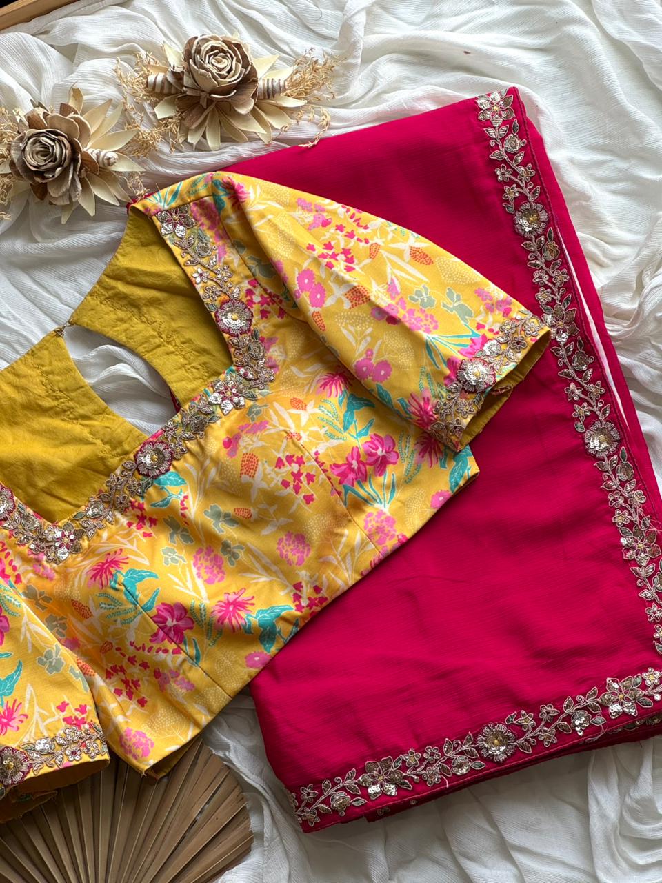 Yellow blouse with floral patterns and pink saree with intricate border on a white surface.