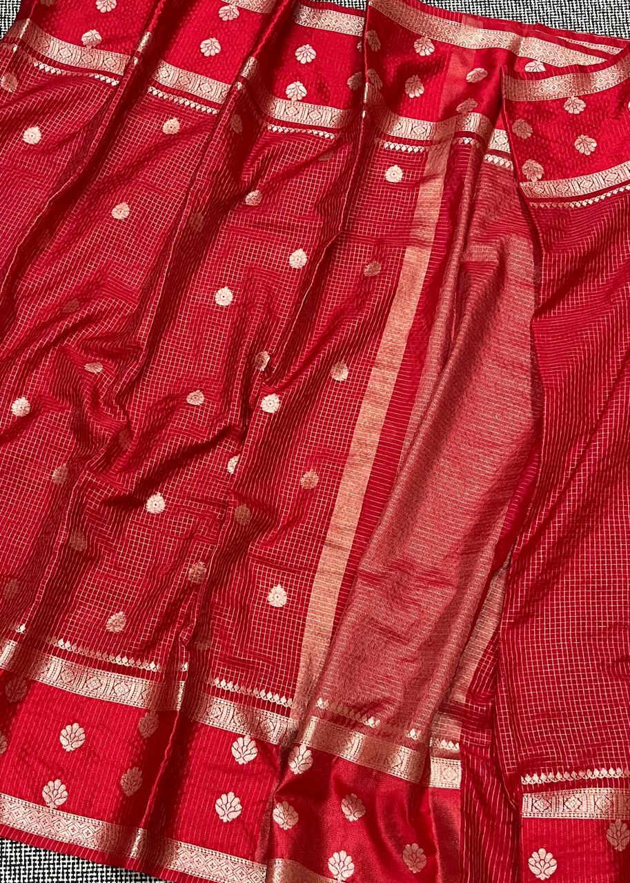 Red saree with white patterns and gold border on a checkered fabric background