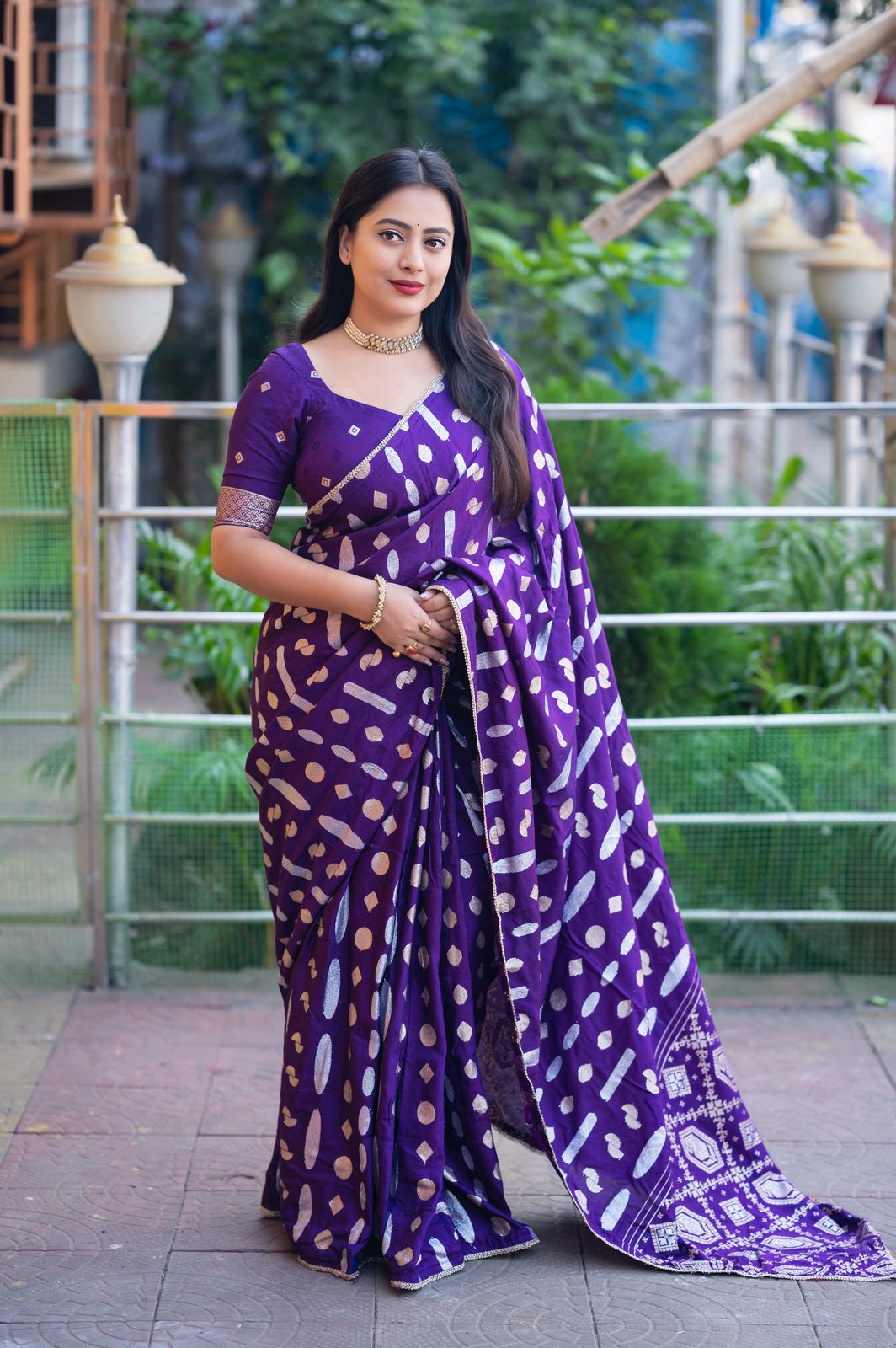 Woman wearing a purple saree with white patterns outdoors.