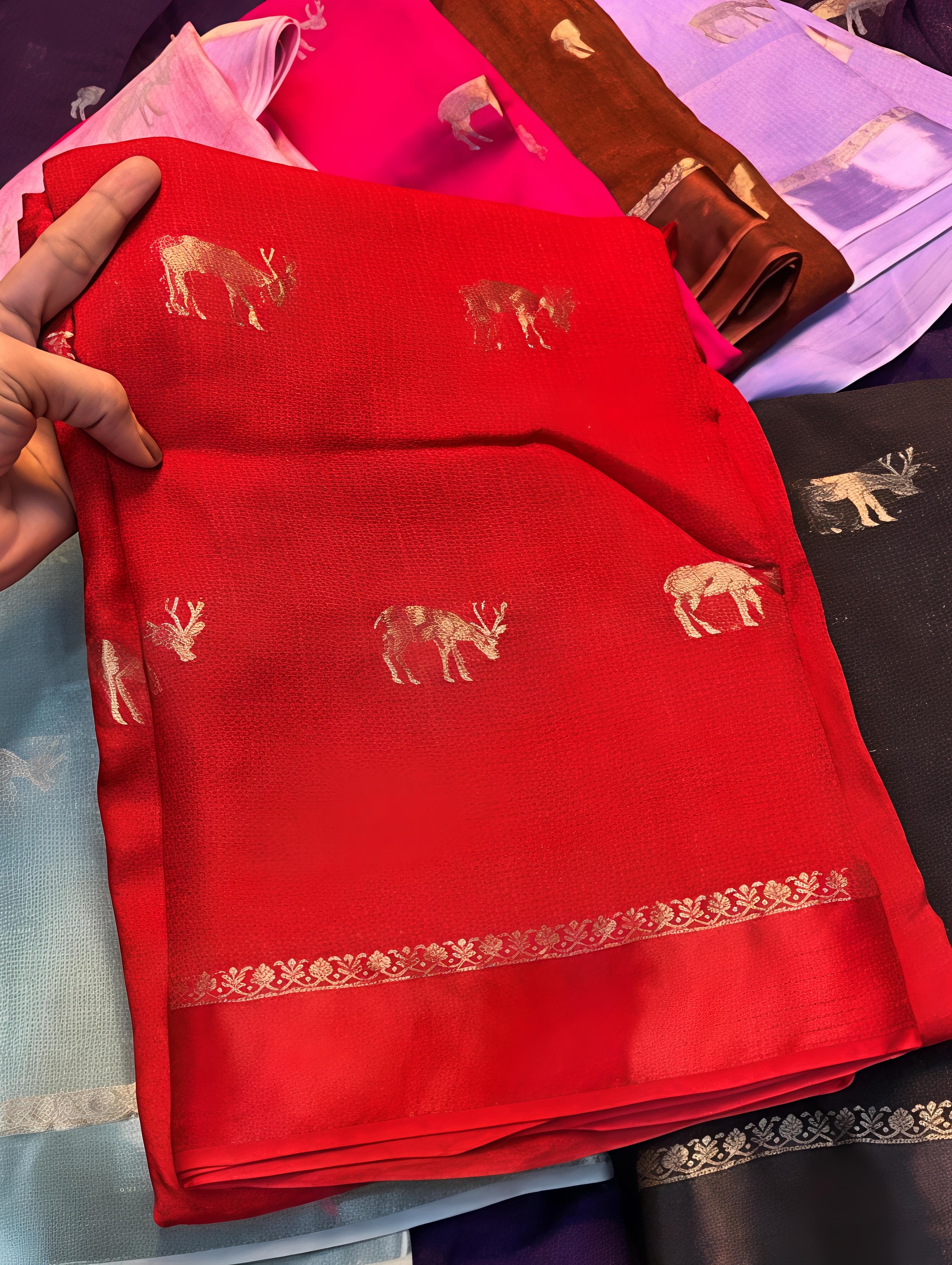 Red fabric with deer patterns held by a hand, with other fabrics in the background.