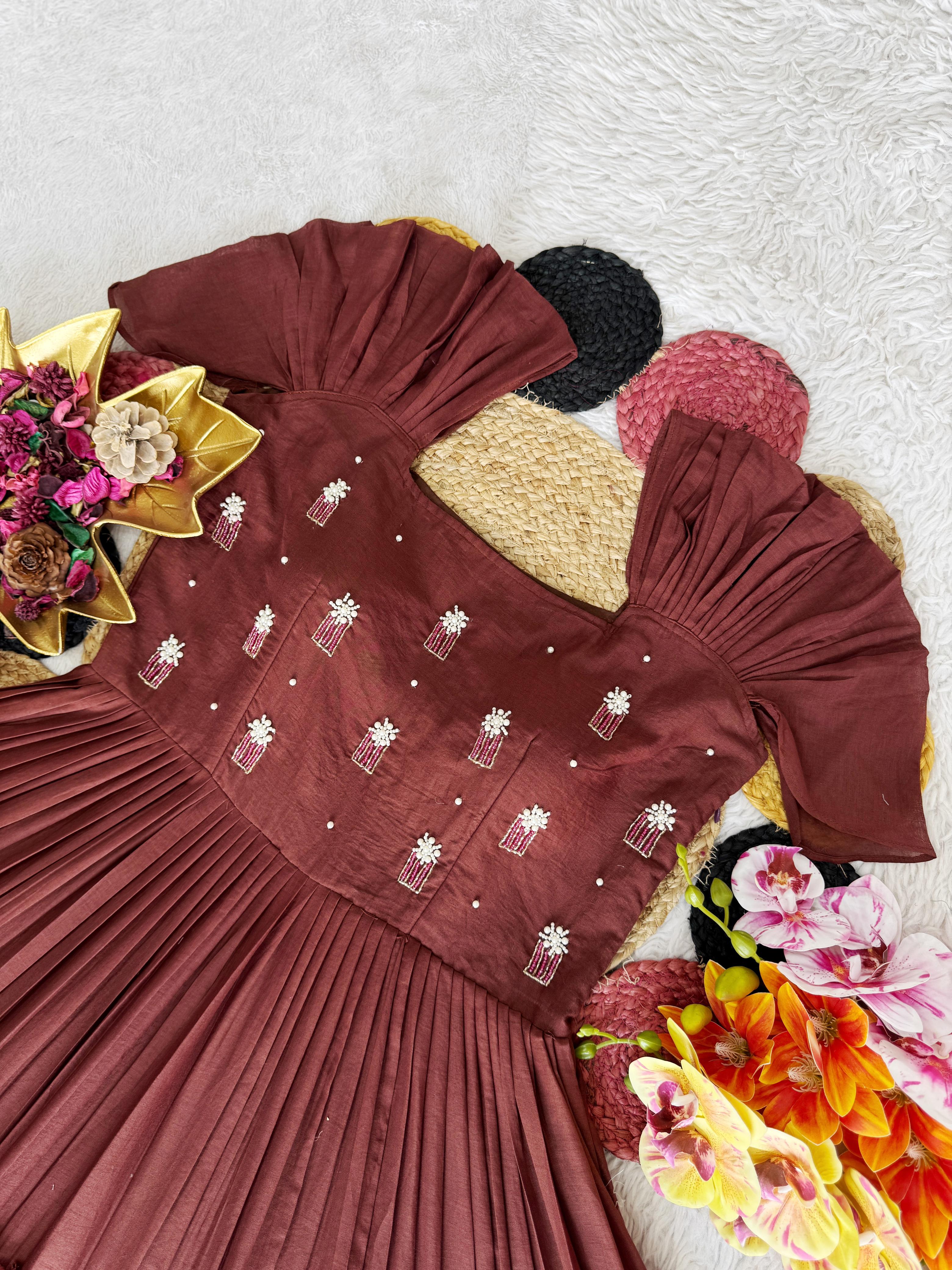 Brown pleated dress with floral embellishments on a textured surface with decorative items.