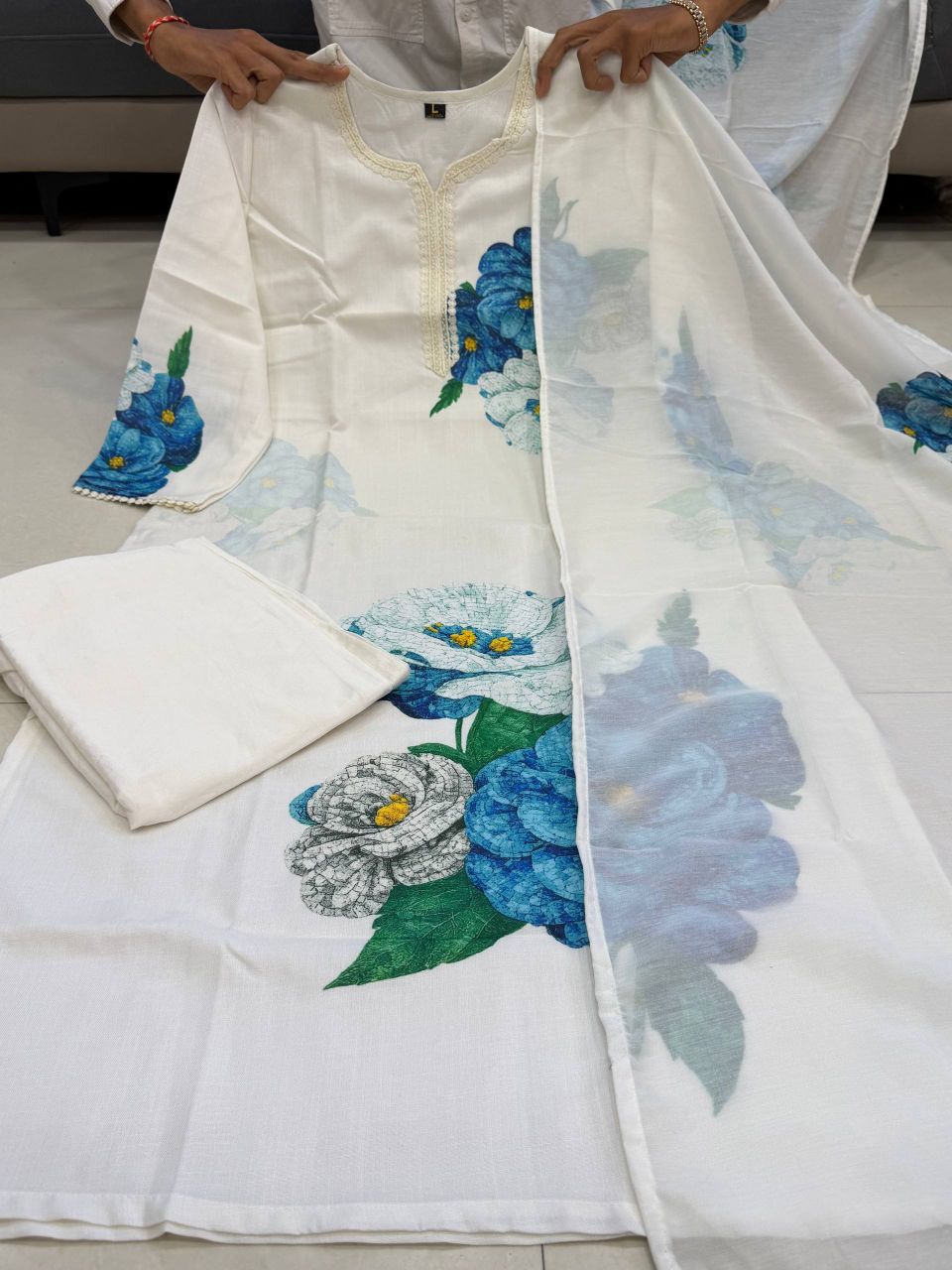 White fabric with blue floral embroidery held by a person on a tiled floor.