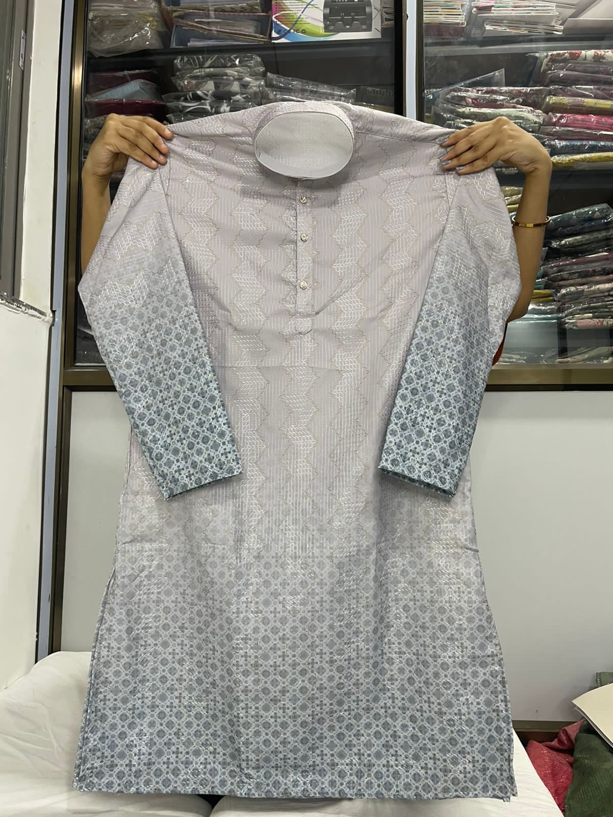 Gray kurta with blue floral patterns on sleeves held up against a store background