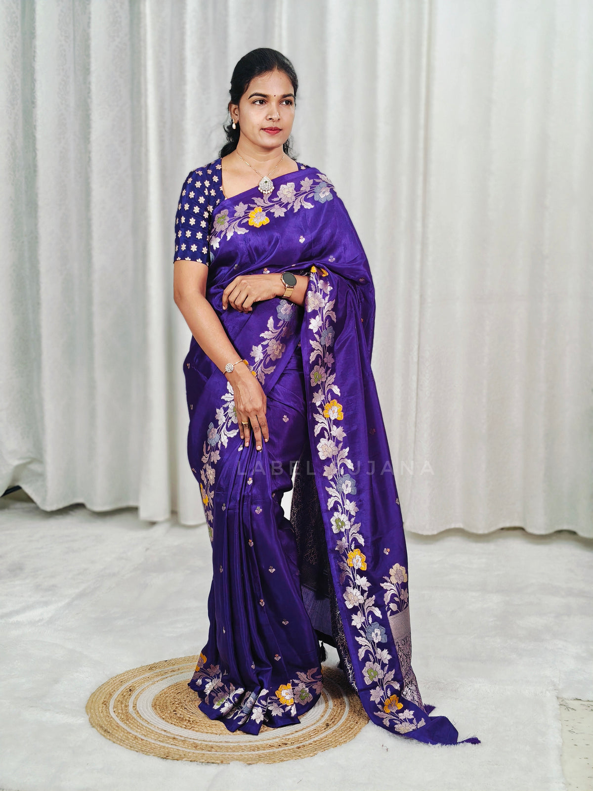 A woman modeling a purple silk saree with floral embroidery and a matching embroidered blouse