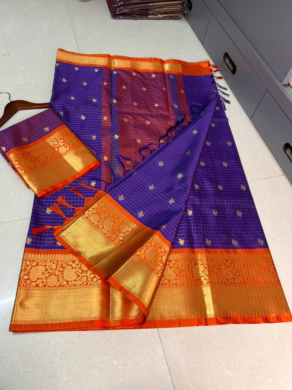 Purple and orange saree with gold border on a white floor.