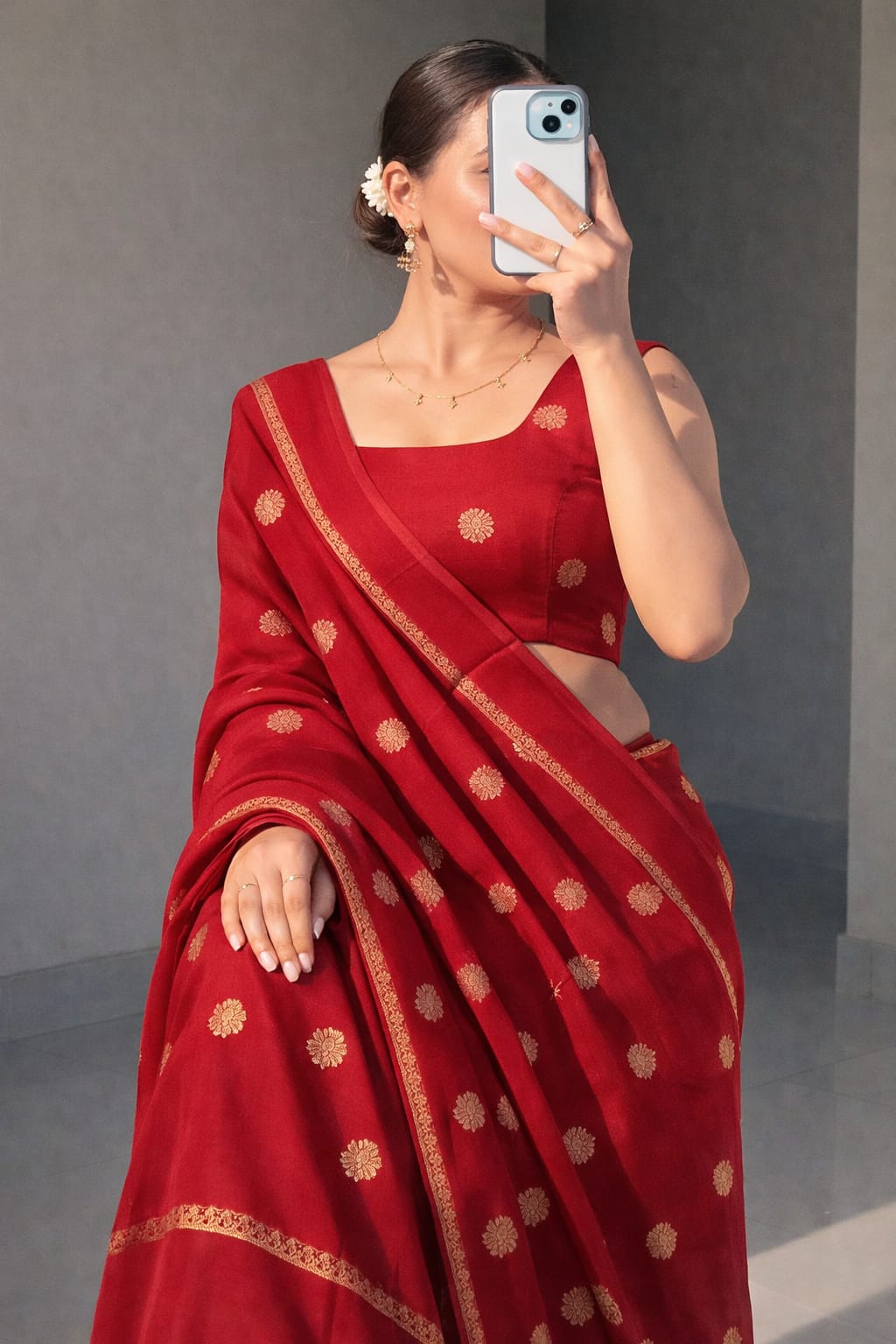 Woman wearing a red saree with gold patterns, taking a mirror selfie.