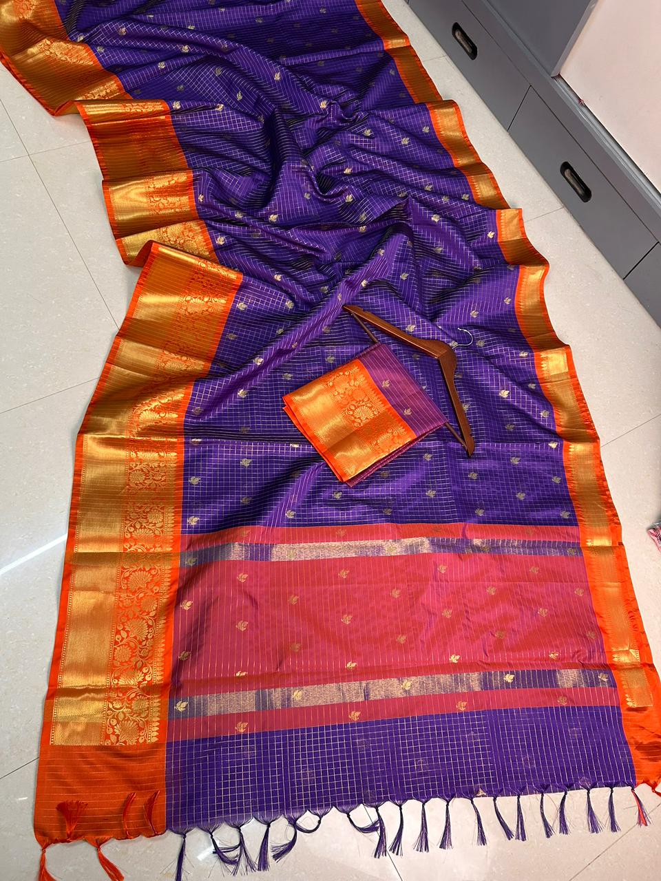 Purple and orange saree with gold border on a white floor.