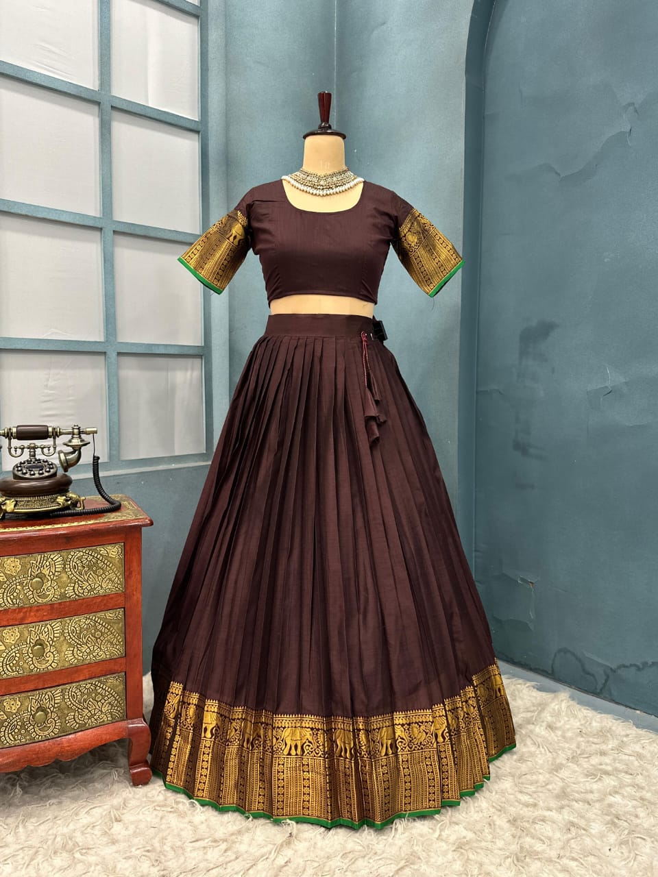 Brown traditional outfit with gold details on a mannequin against a blue wall.