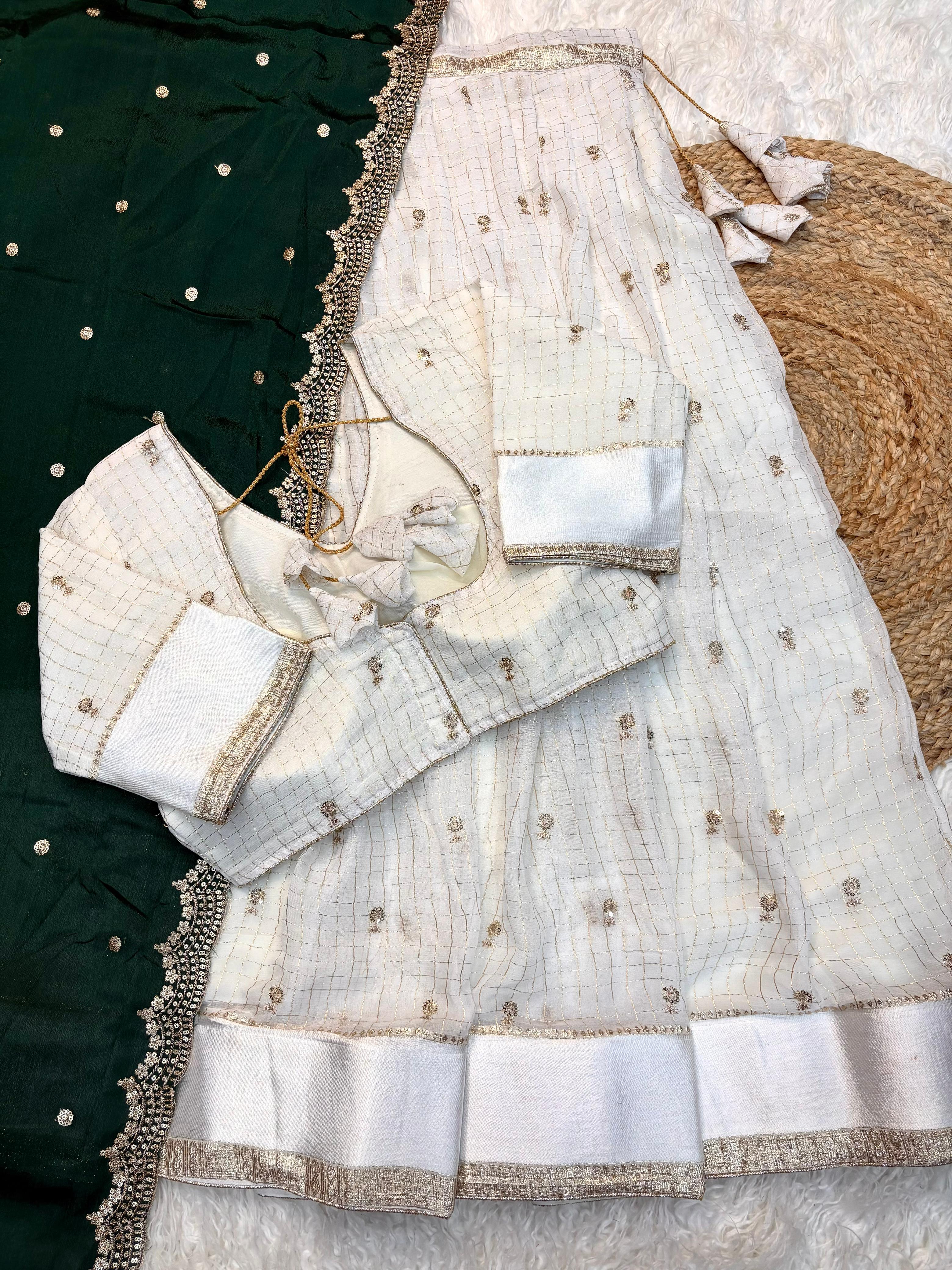 White embroiderey blouse with dark green saree with gold details on a texture surface
