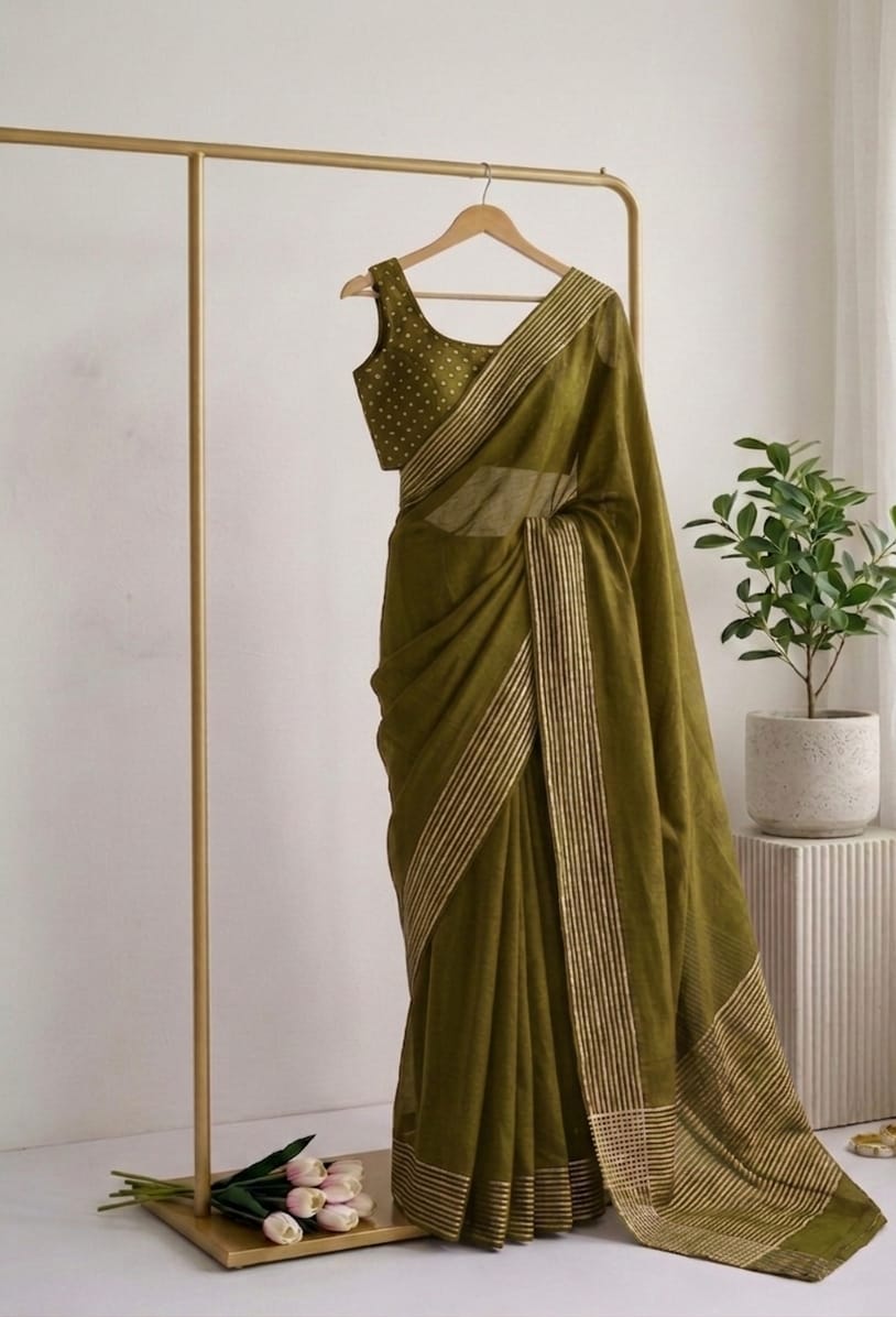 Olive Green saree with a blouse on a hanger against a white wall with a plant in the background.