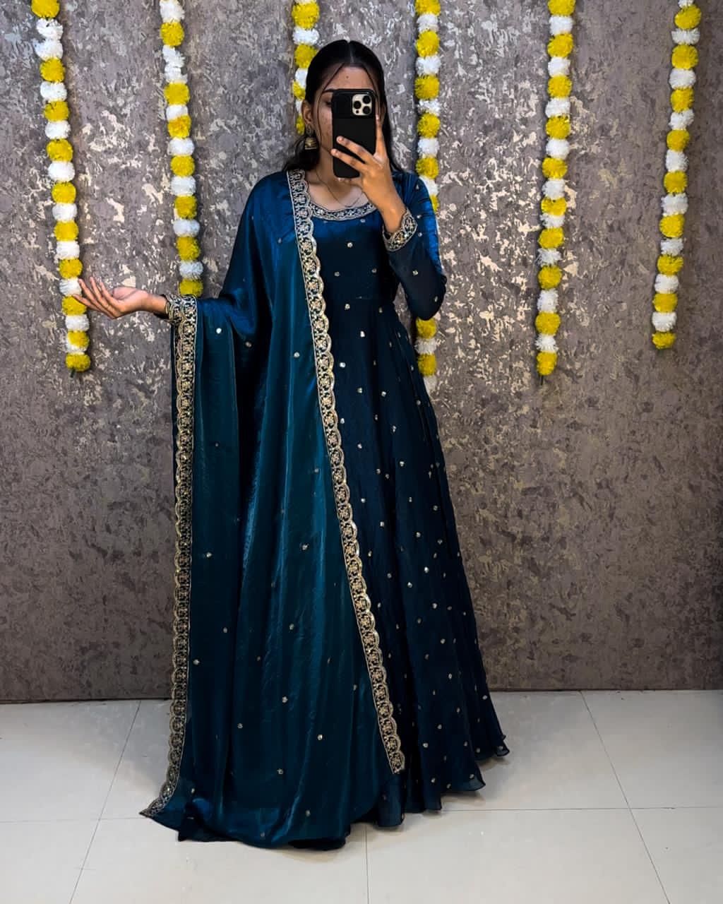 Woman in a Teal blue traditional outfit with gold details, standing against a decorative wall.