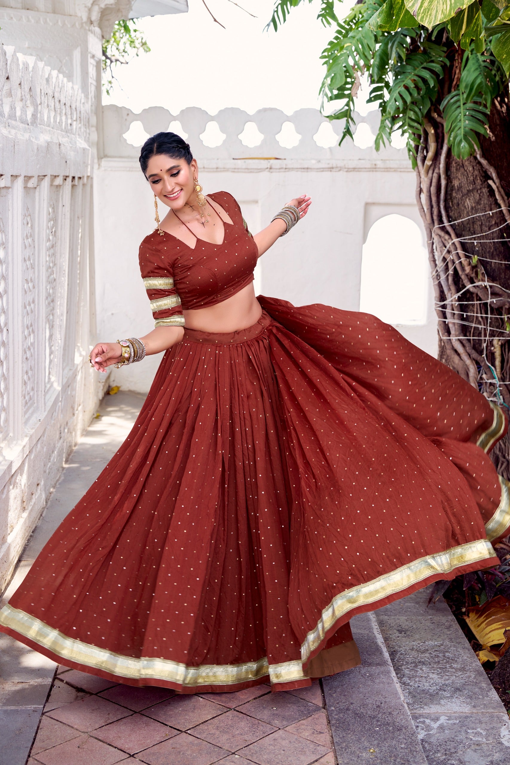 Woman in a traditional maroon saree with gold border dancing outdoors.