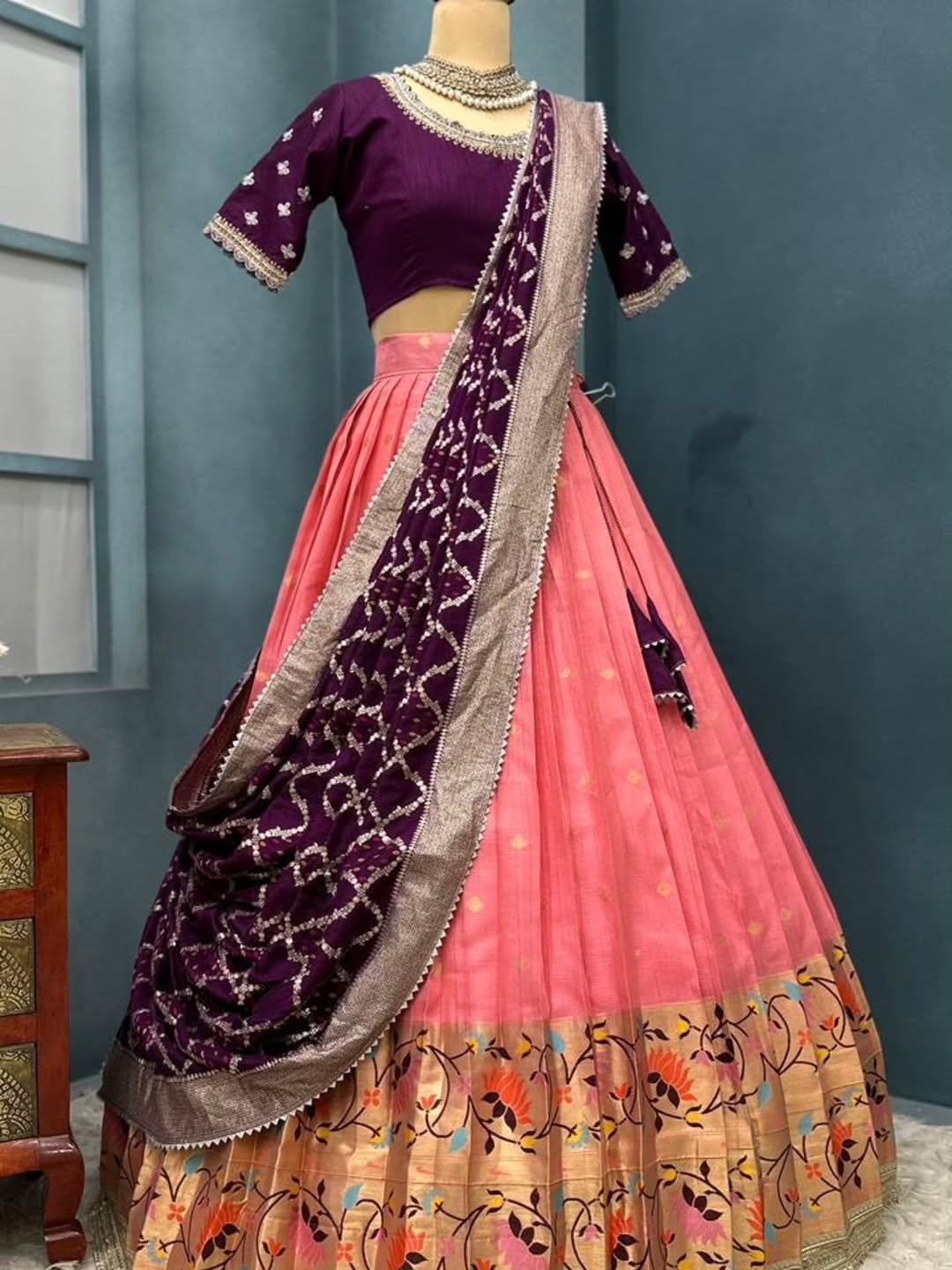 Traditional Indian outfit with peach lehenga and  blouse on a mannequin against a blue wall.