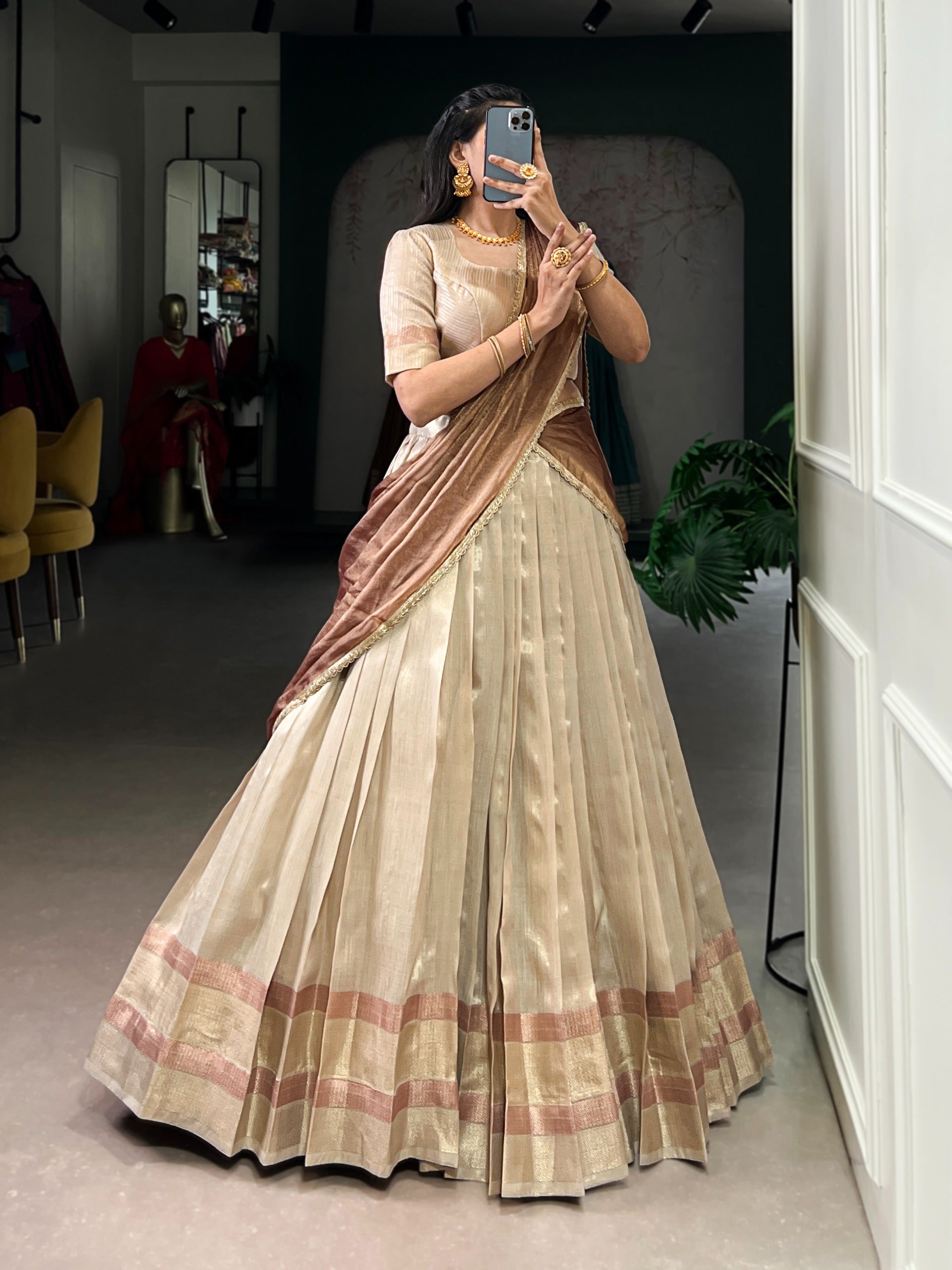 Woman wearing a cream traditional saree in a room with a mirror and plant.