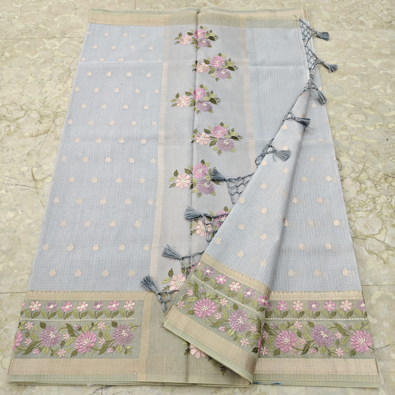 Light blue fabric with floral embroidery and tassels on a textured surface