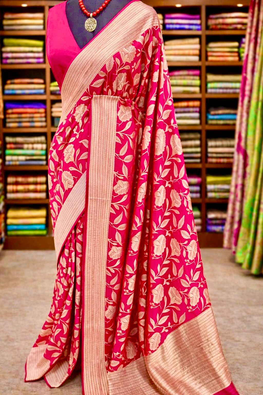 Vibrant Pink saree with floral patterns displayed against a background of colorful sarees.
