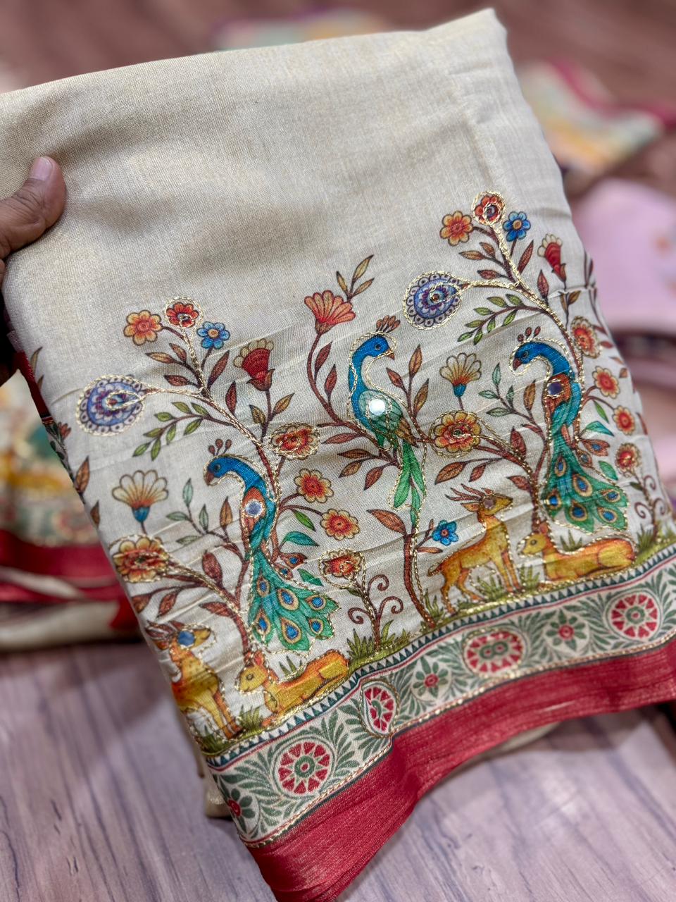 Cream fabric with intricate peacock and floral design on a wooden surface