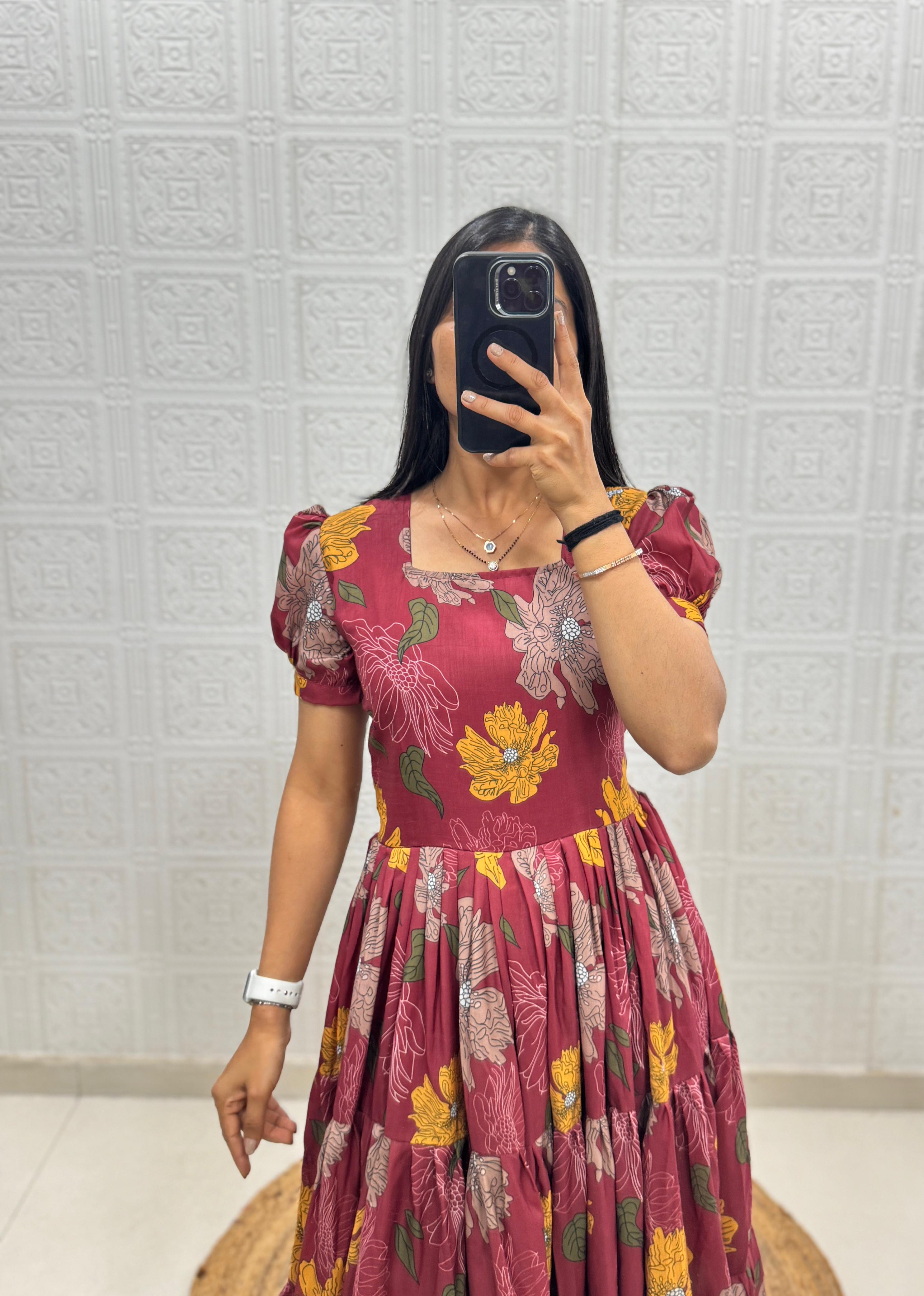 Person wearing a maroon floral dress taking a mirror selfie against a textured white wall.