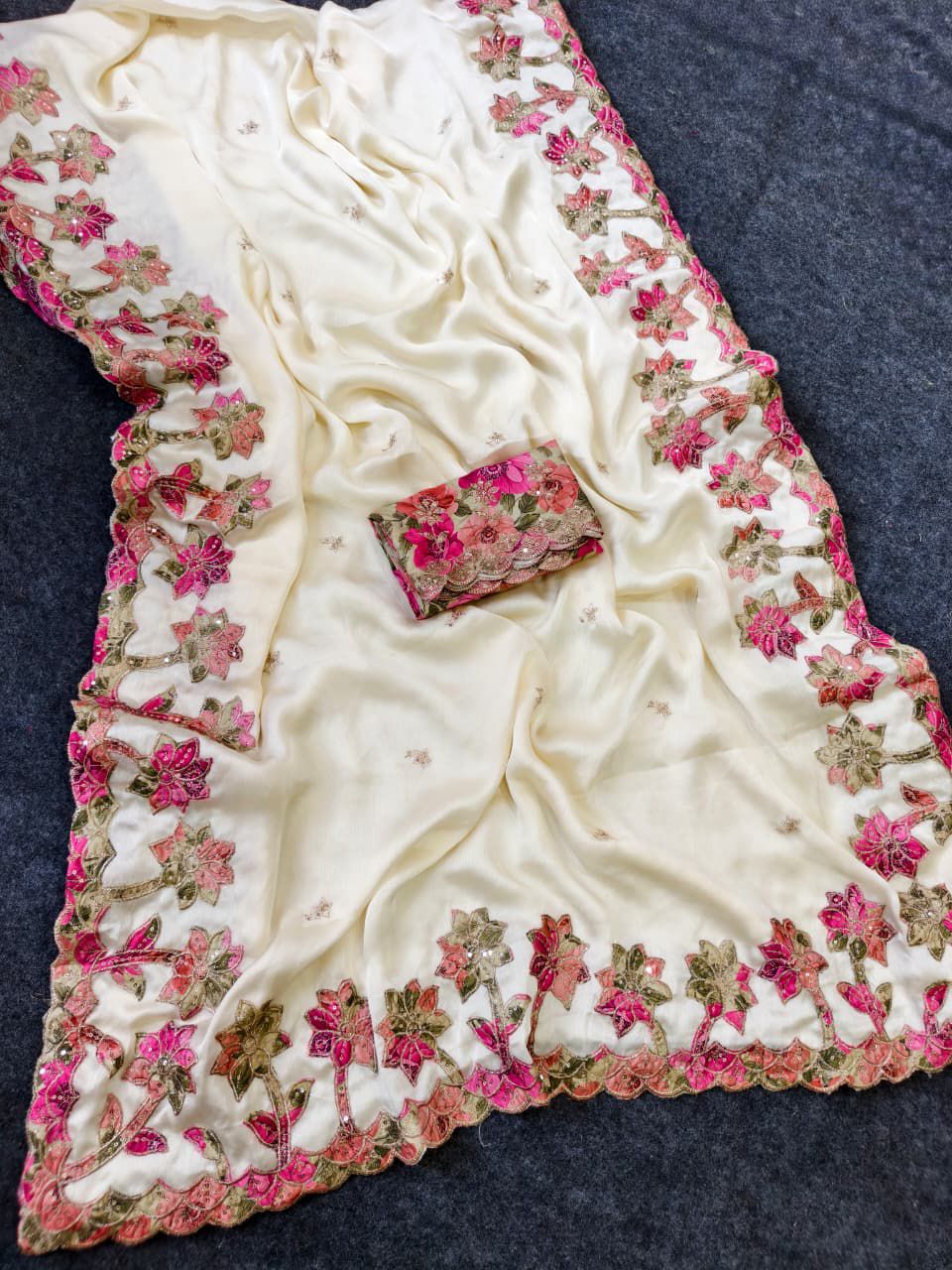 White saree with pink floral embroidery on a dark background