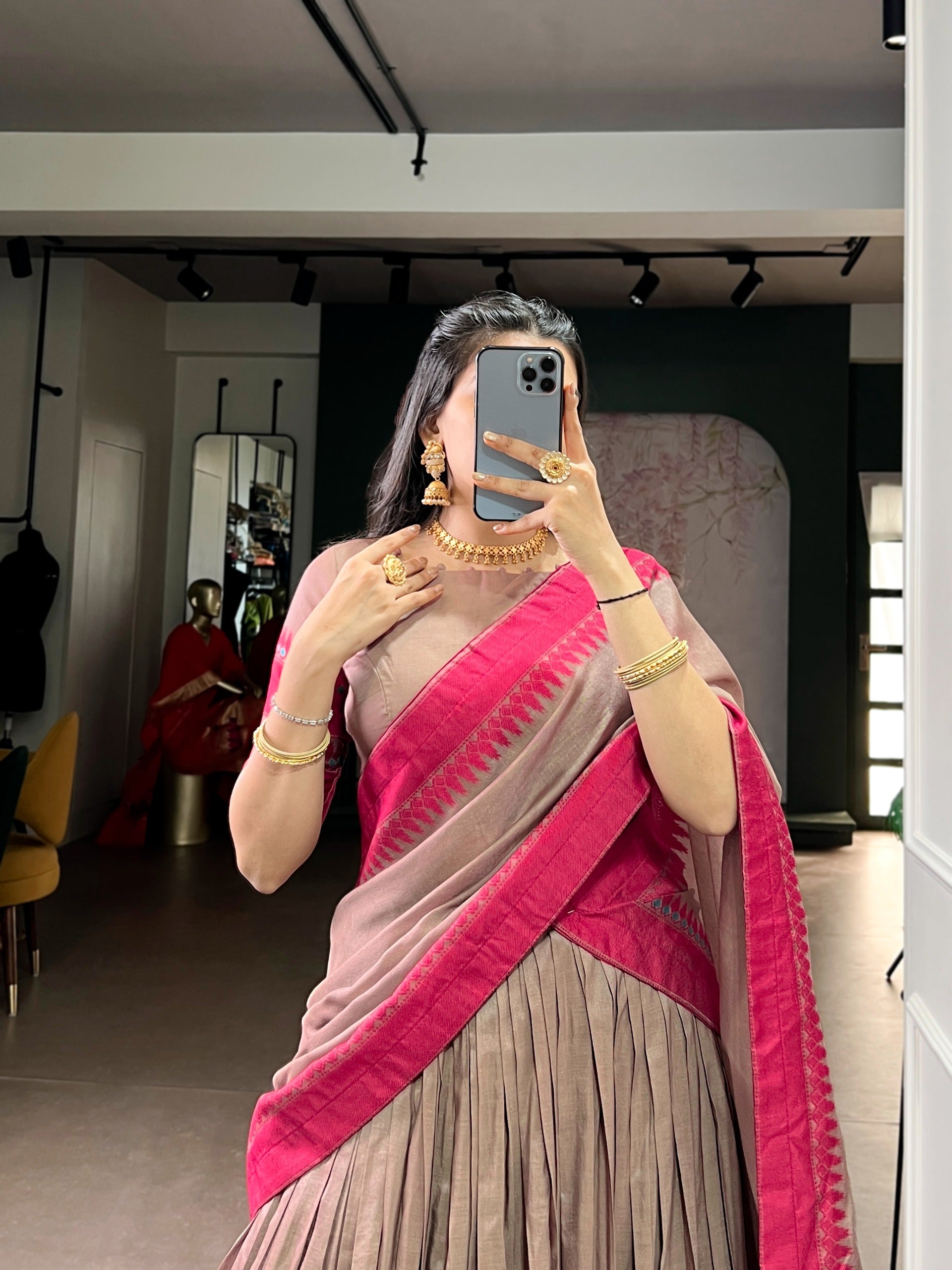 Woman wearing a copper saree with gold jewelry in a room.