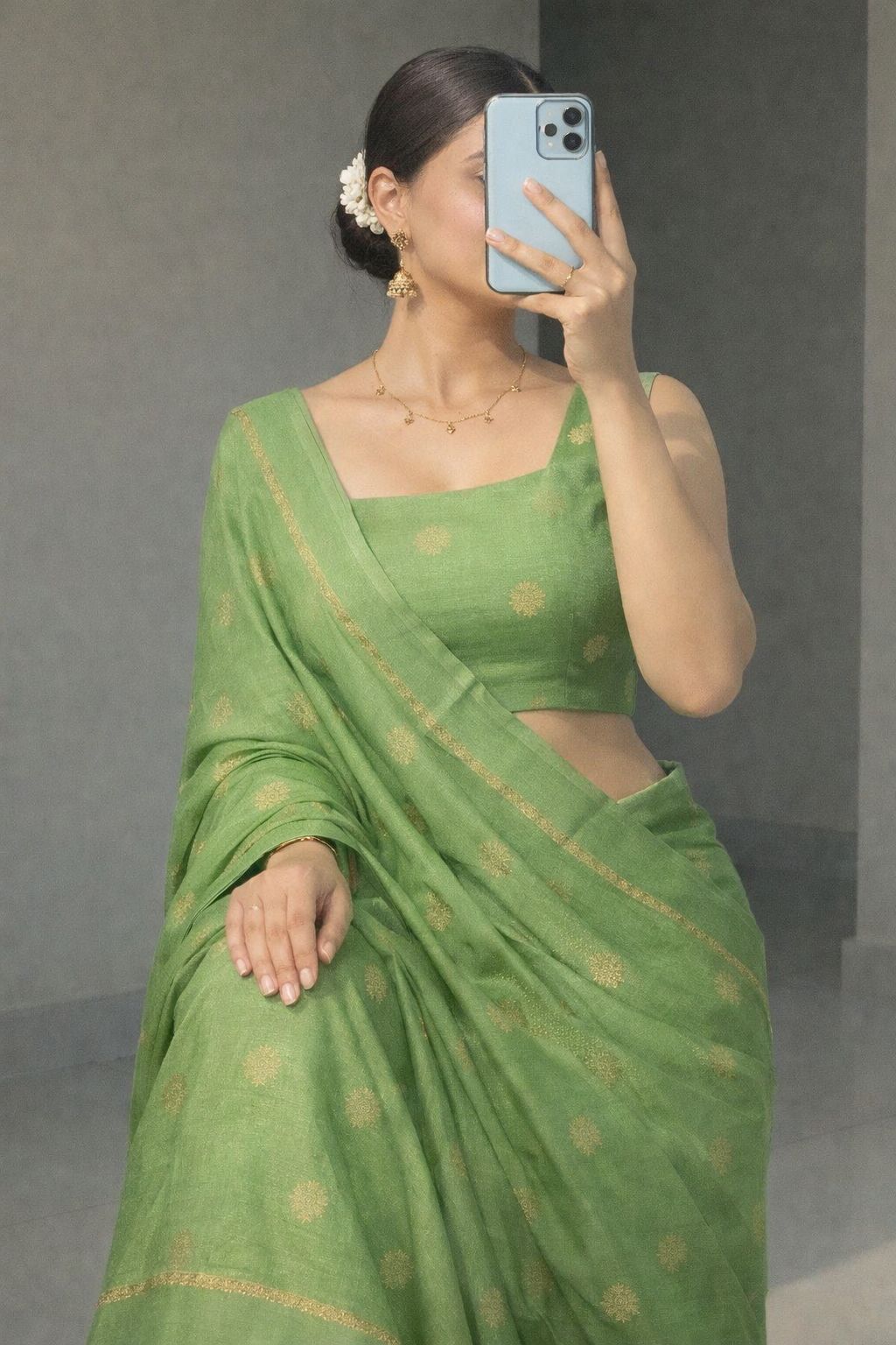 Woman wearing a light green saree with gold patterns, holding a phone to her ear against a gray background.