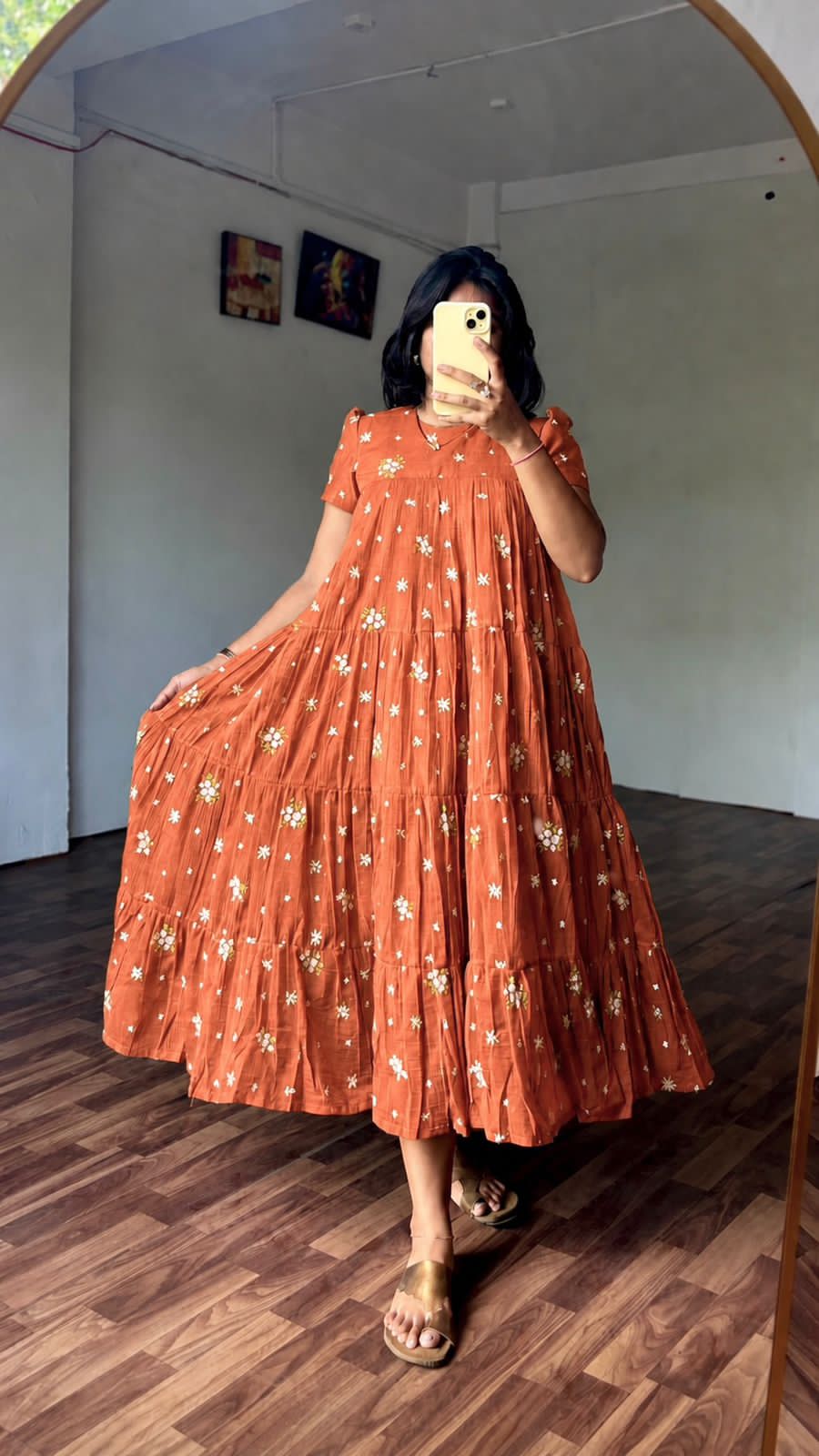 Person wearing a long orange dress with floral patterns in a room with wooden flooring.