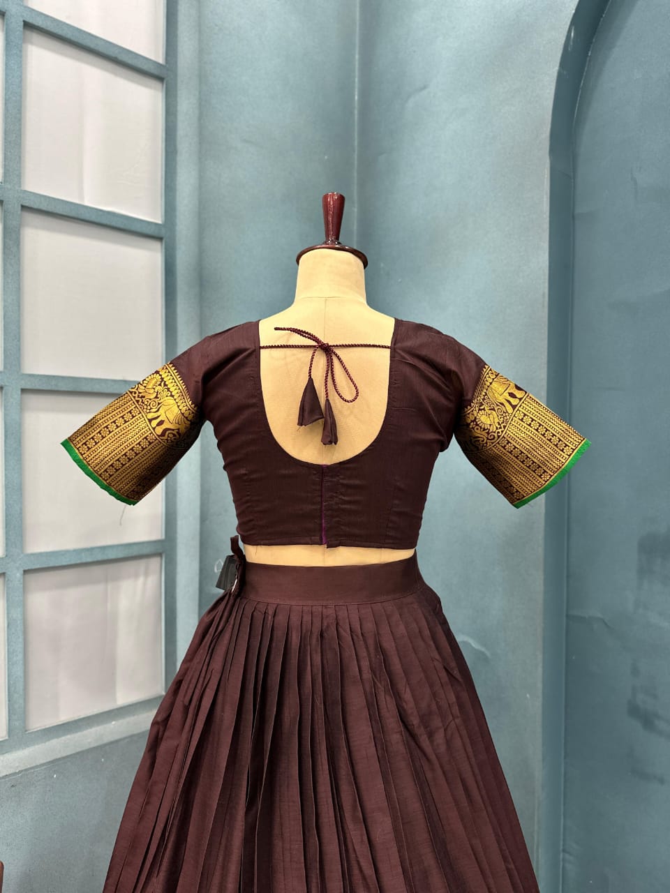 Brown traditional outfit with gold sleeves on a mannequin against a light blue wall.
