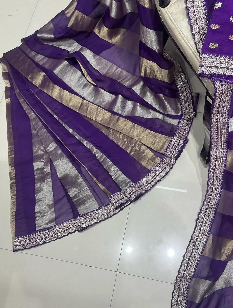 Purple and gold saree with intricate patterns on a white floor.