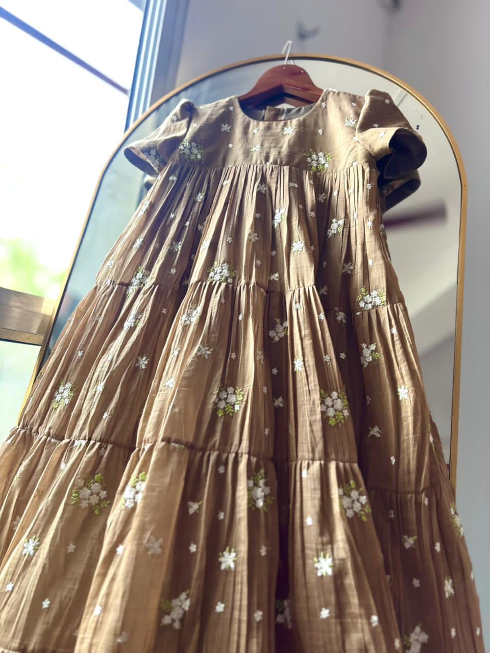 Chiko dress with floral patterns on a hanger in front of a mirror.