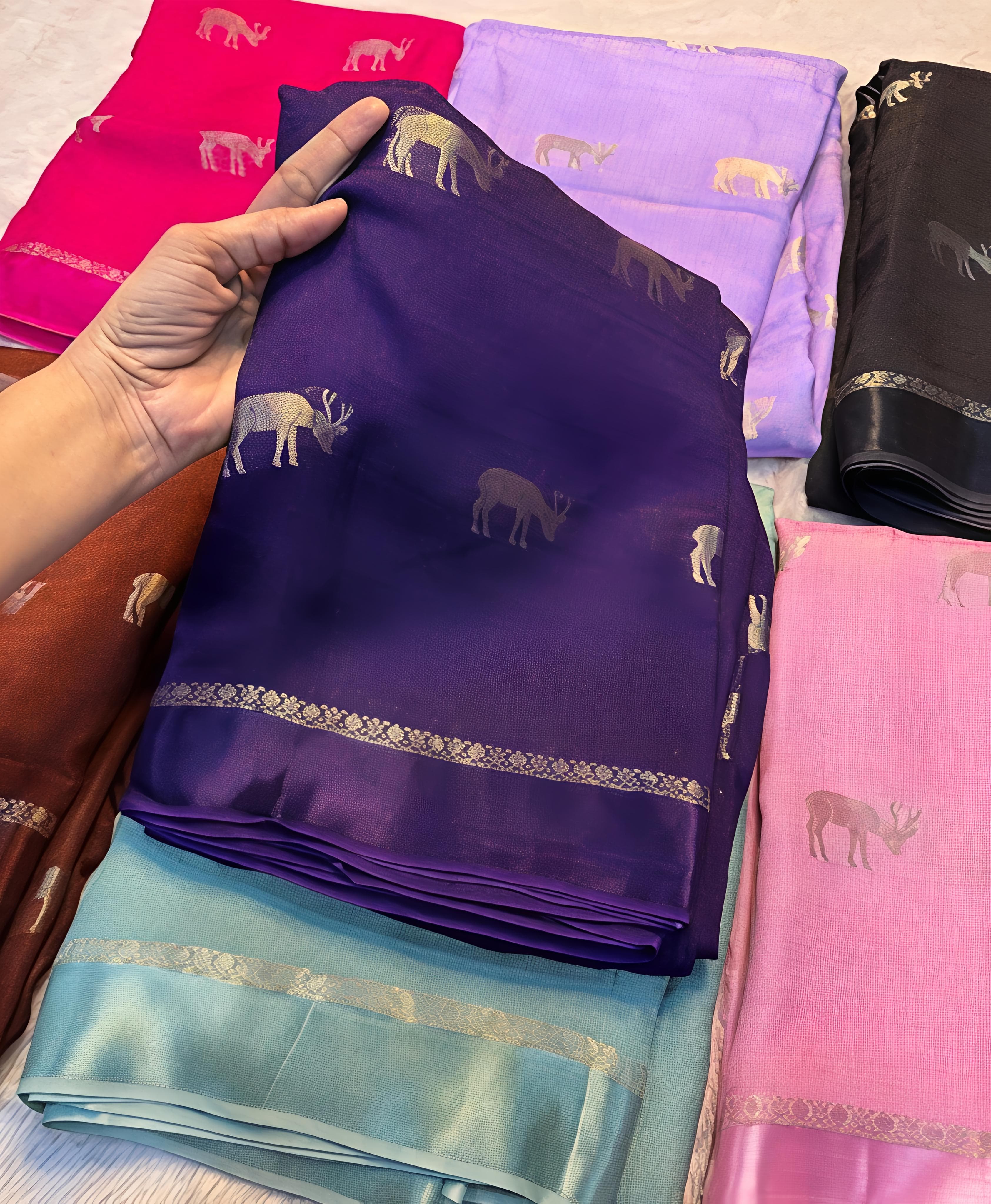 Hand holding a purple saree with animal patterns among other colorful sarees.