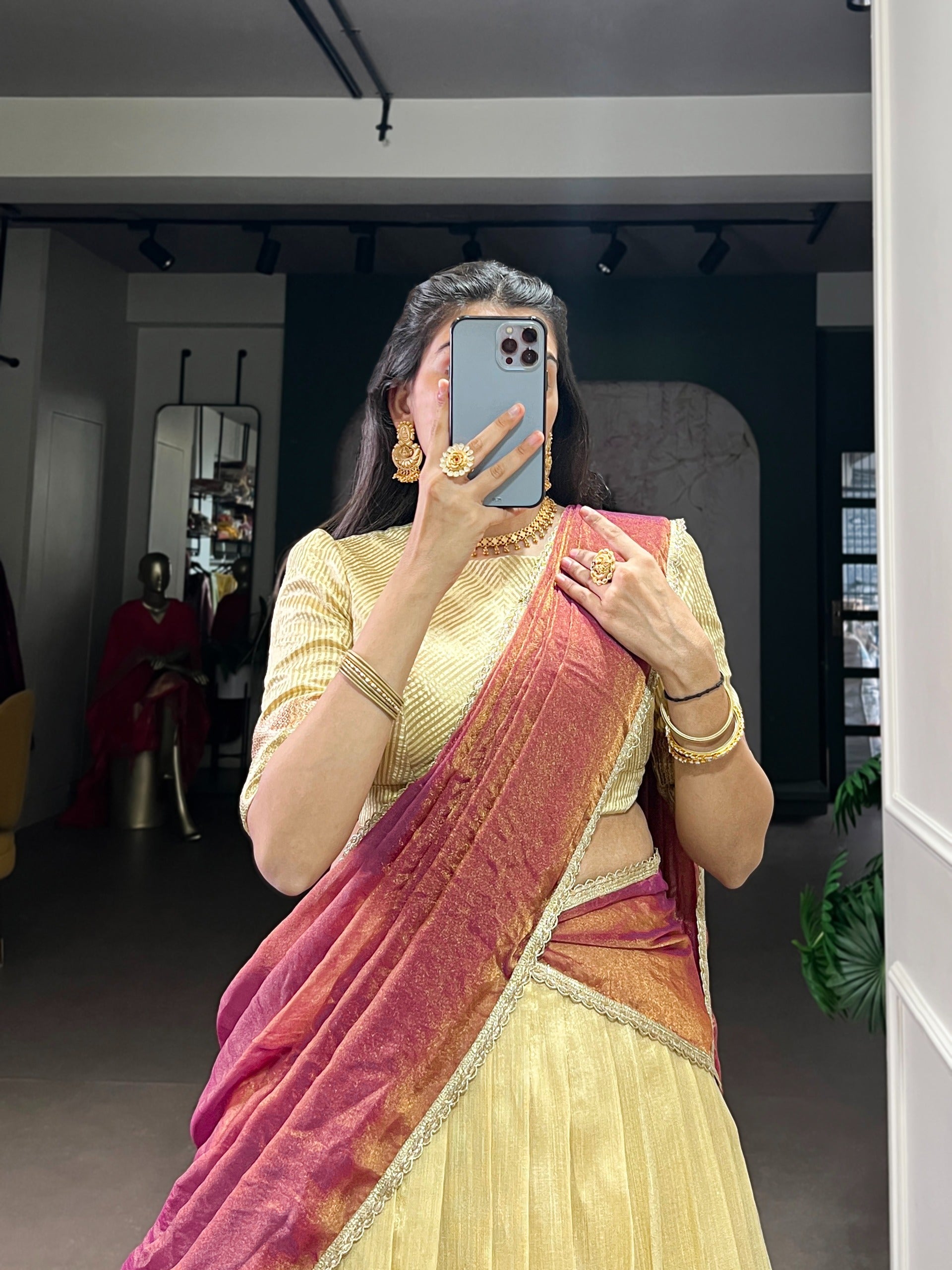 Woman taking a mirror selfie wearing a Beige colour traditional saree in a room.