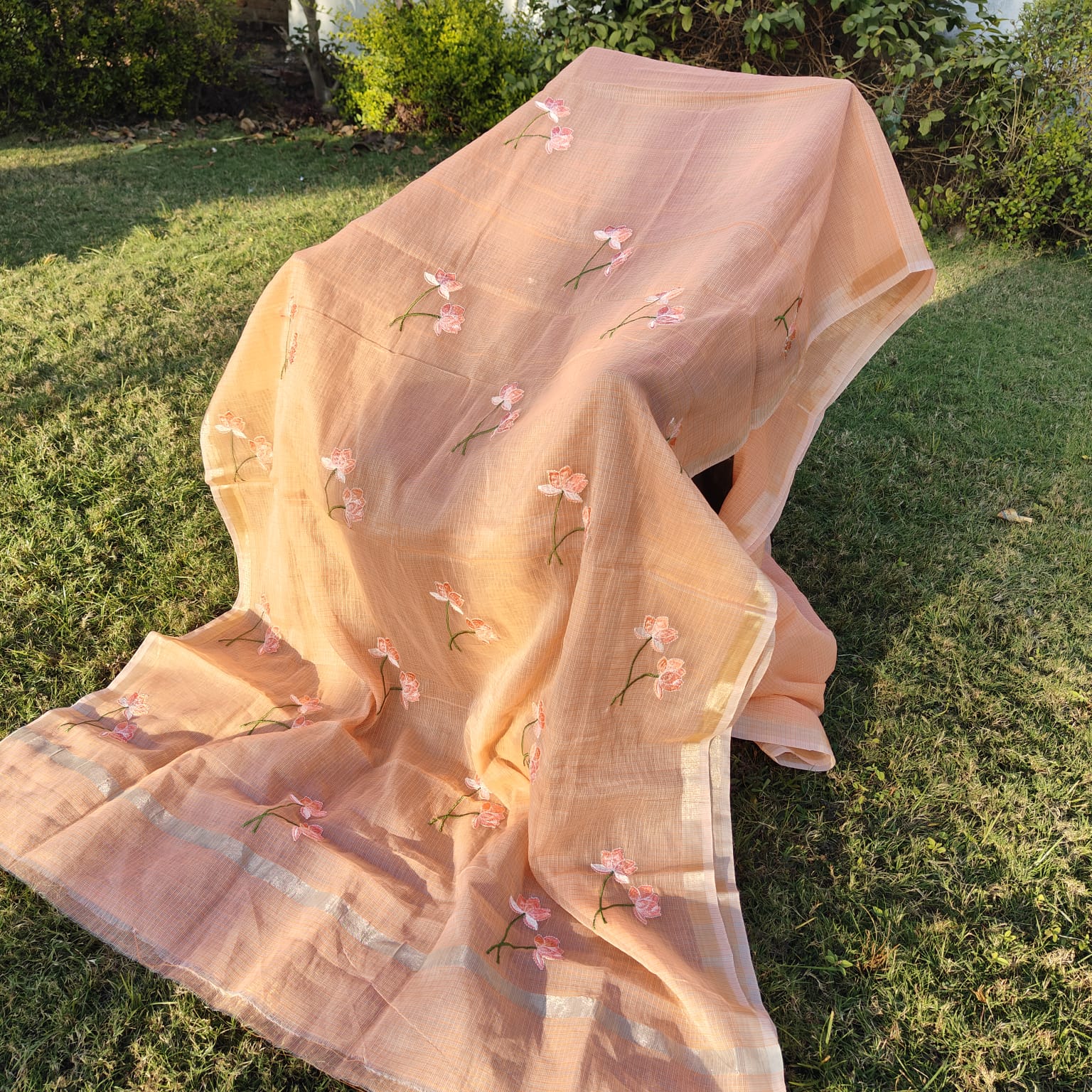 Peach scarf with floral embroidery on a grassy background