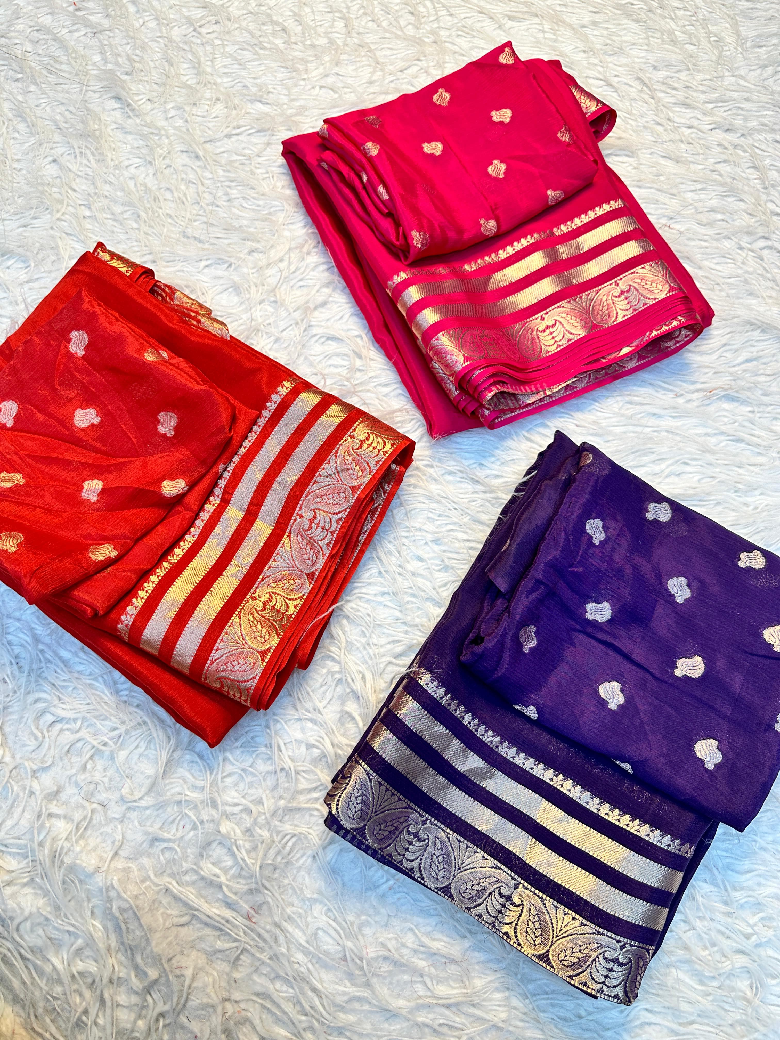 Three folded sarees in red, pink, and purple with gold border 