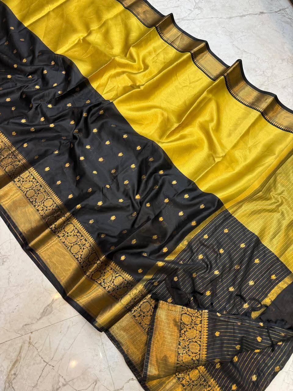 Black and yellow saree with gold patterns on a marble floor