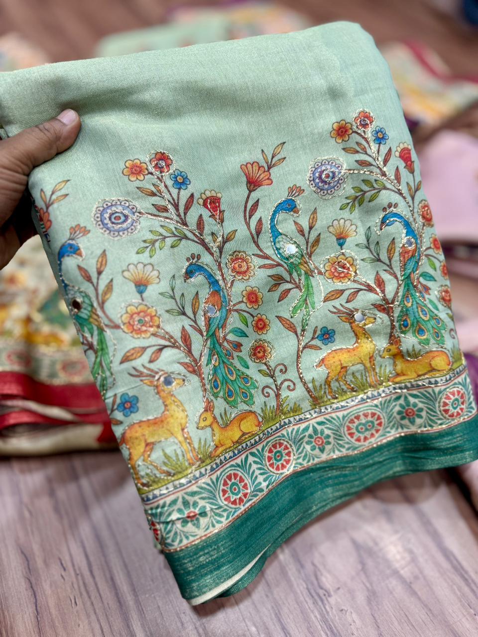 pista green saree and floral patterns held by a hand on a wooden surface.
