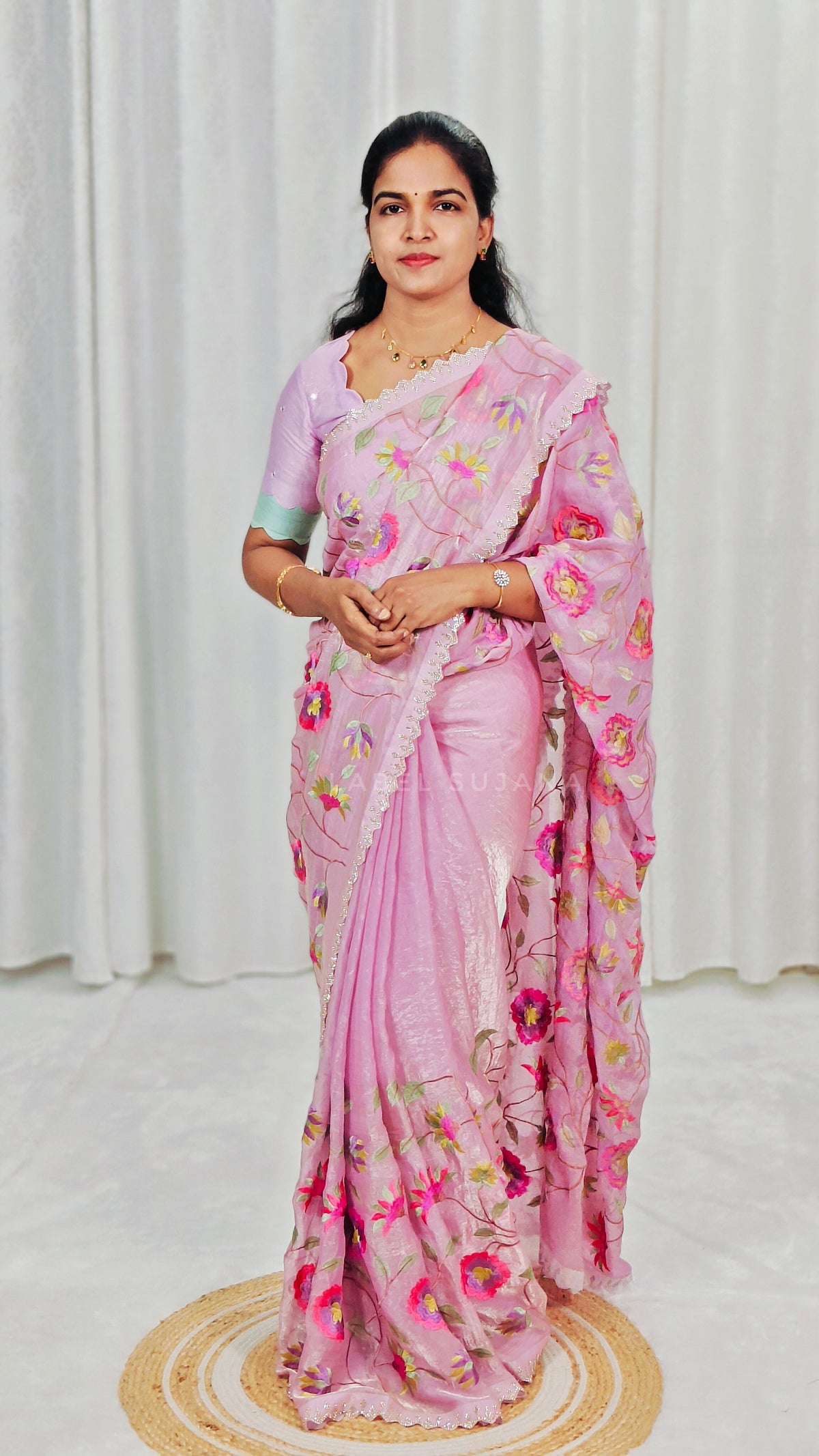 A woman wearing a baby pink saree with colorful floral embroidery and a matching embroidered blouse