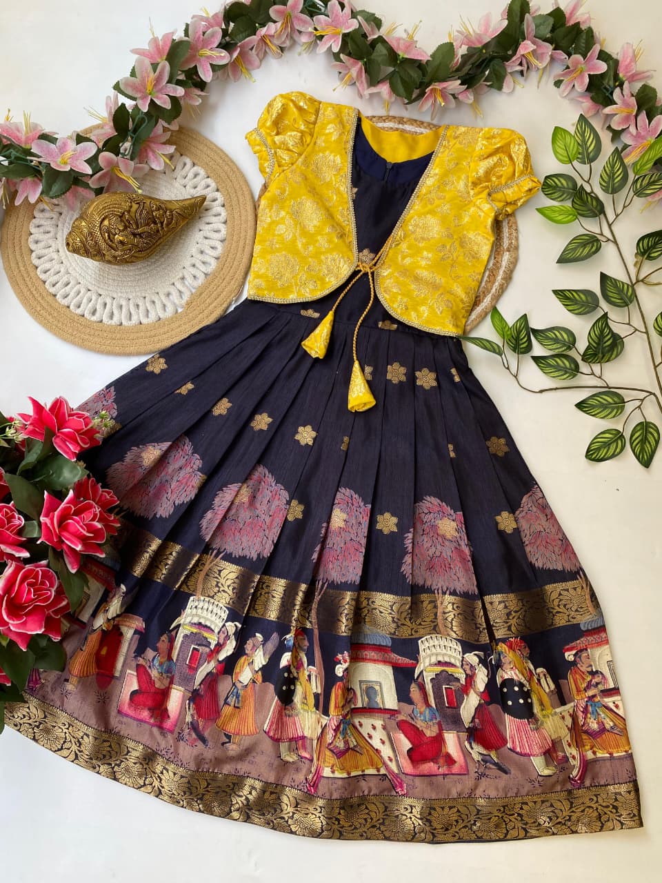 Traditional outfit with yellow blouse and navy blue skirt featuring intricate patterns, surrounded by flowers and leaves.