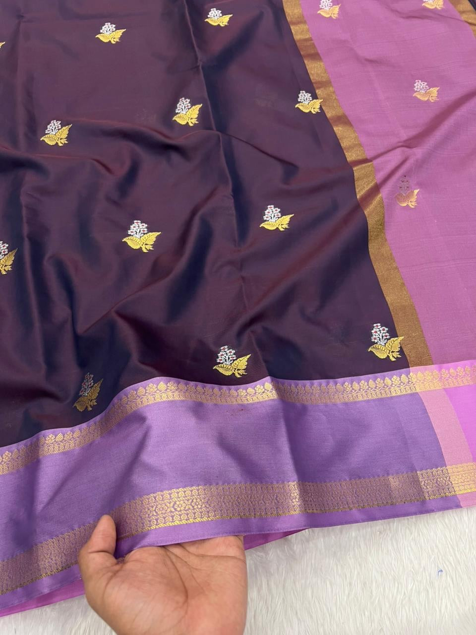 Purple saree with gold border and patterns held by a hand on a white background