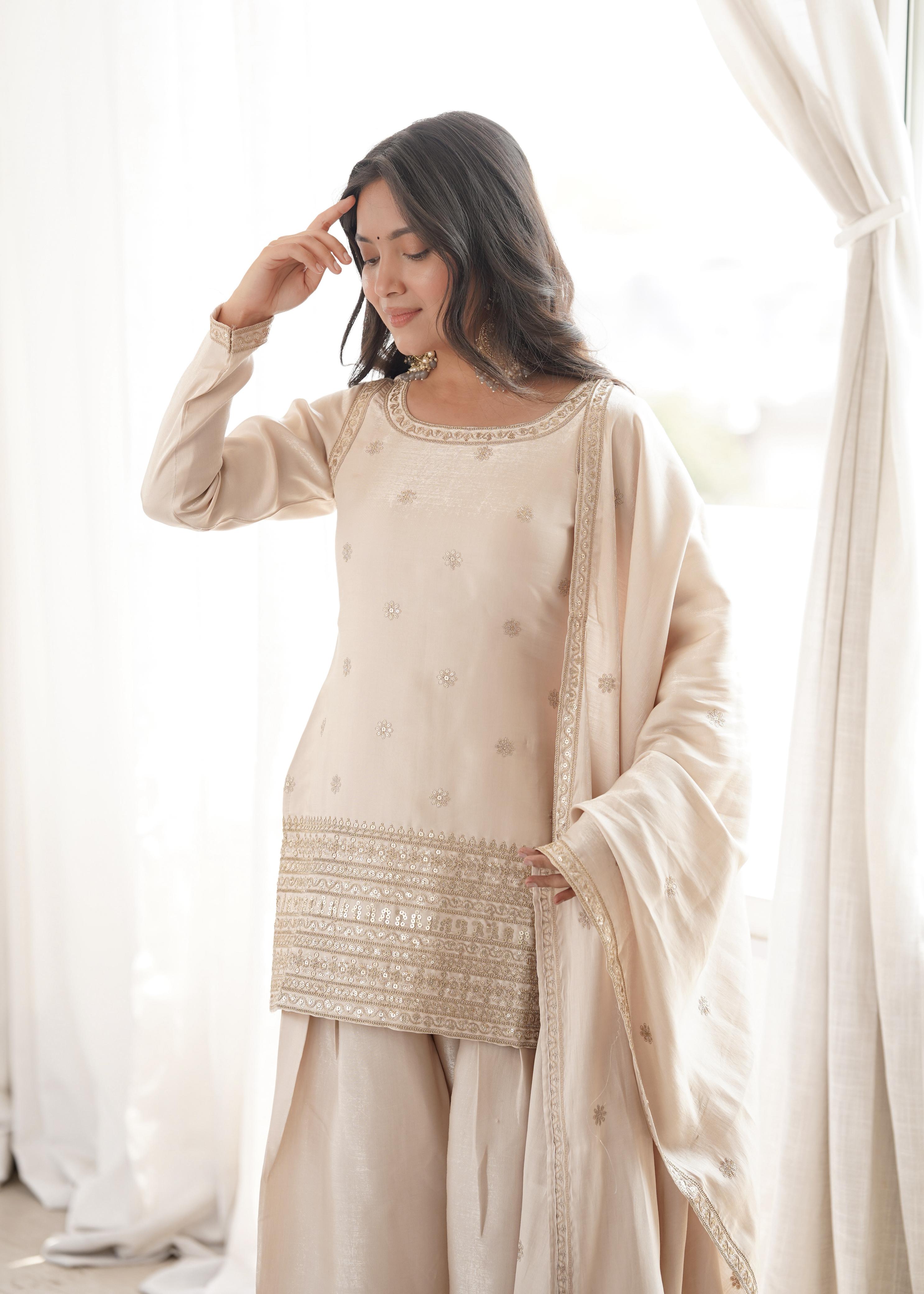 Woman wearing a beige traditional outfit with embroidery in a bright room.