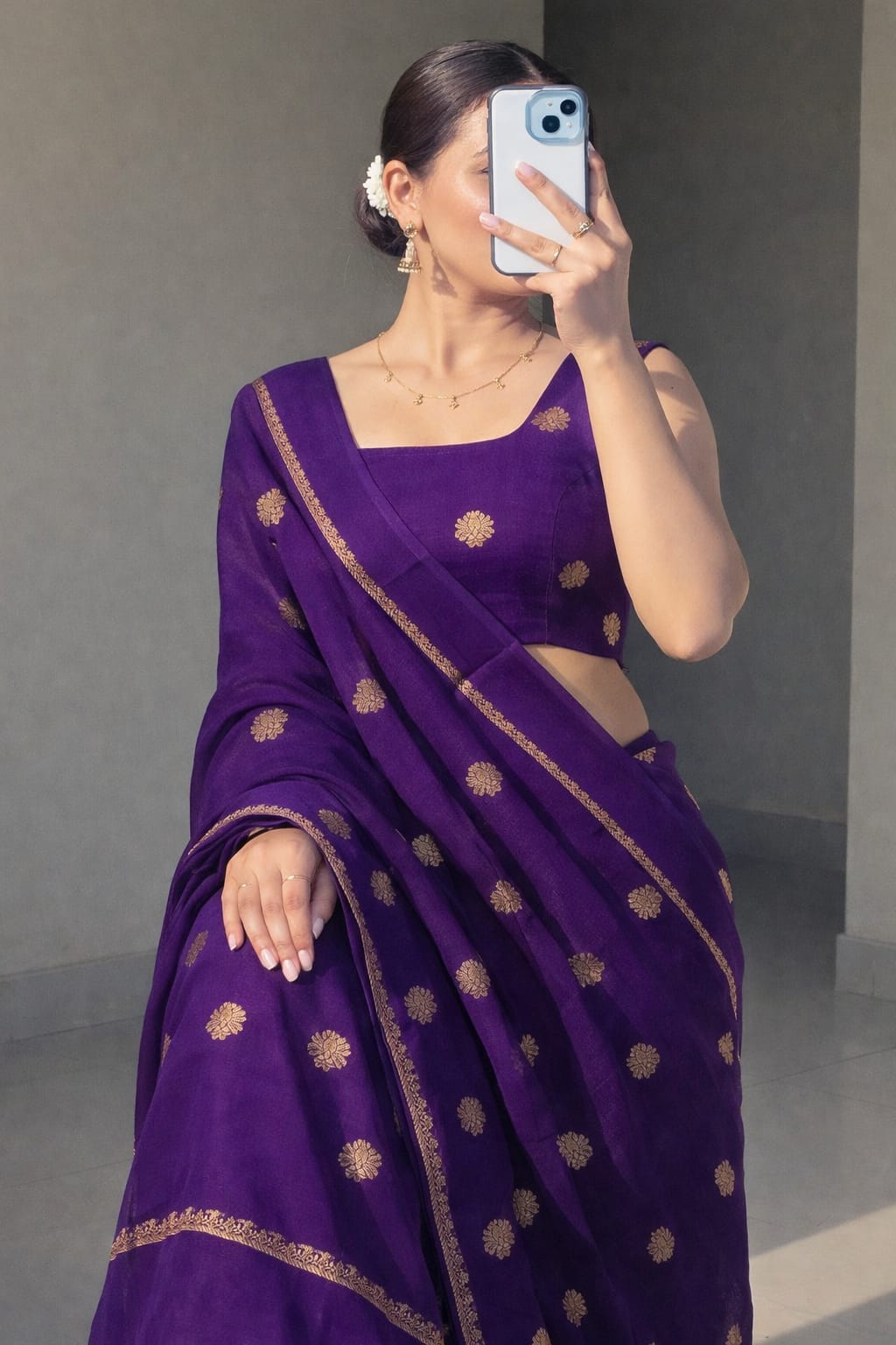 Woman wearing a purple saree with gold patterns, taking a mirror selfie.