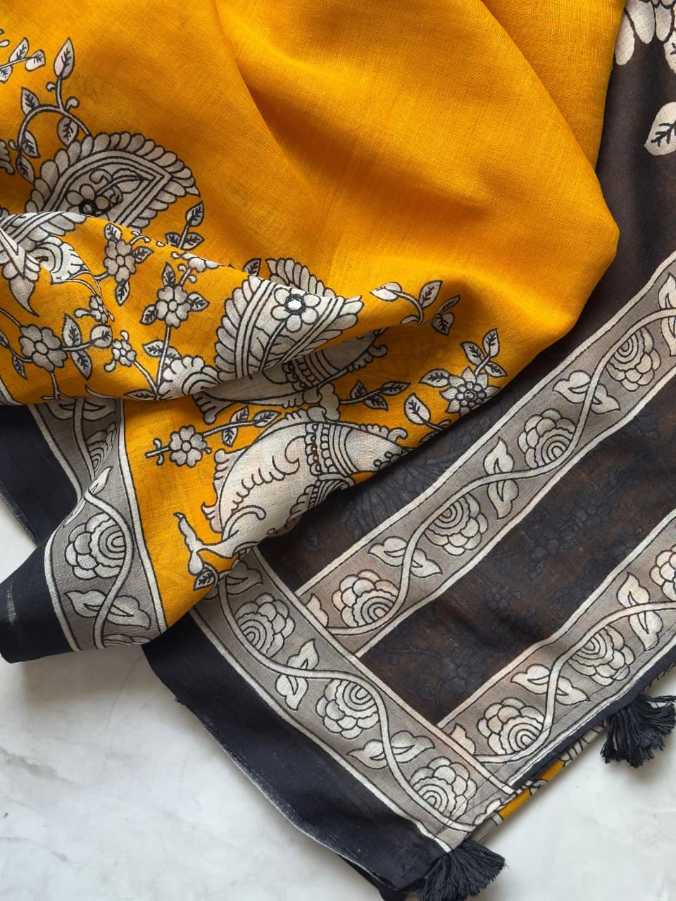 Two patterned scarves, one yellow and one black with white designs, on a marble surface.