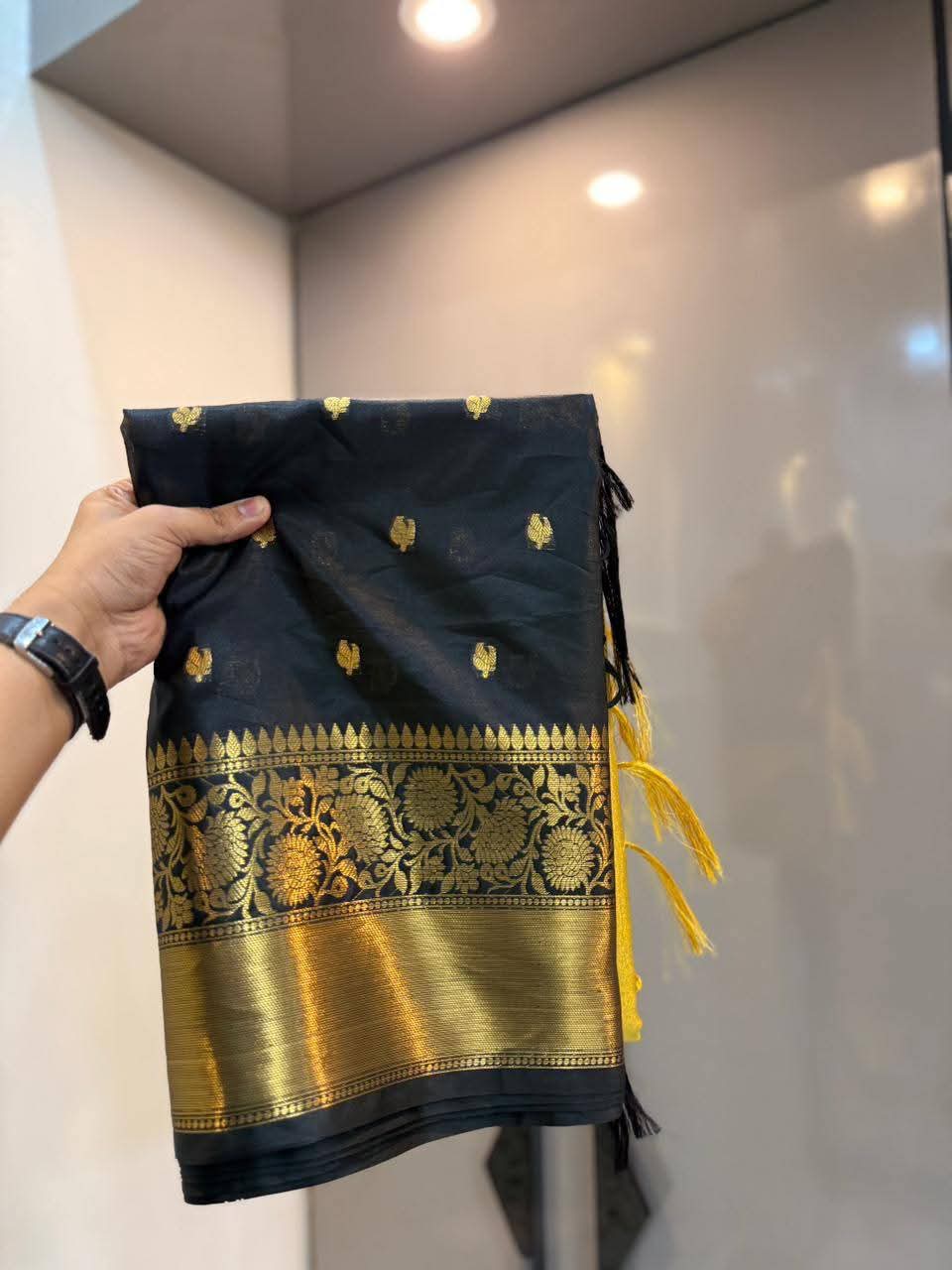 Black and gold traditional fabric held by a hand against a neutral background