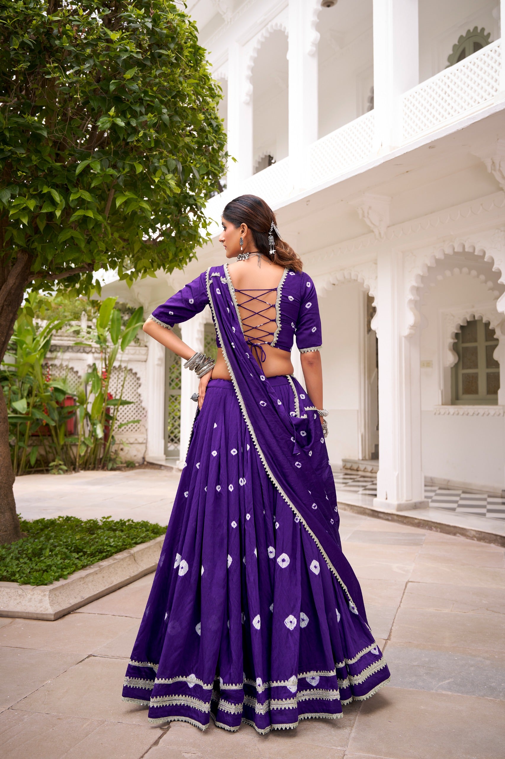 Woman in a purple lehenga with white patterns standing in front of a white architectural building.