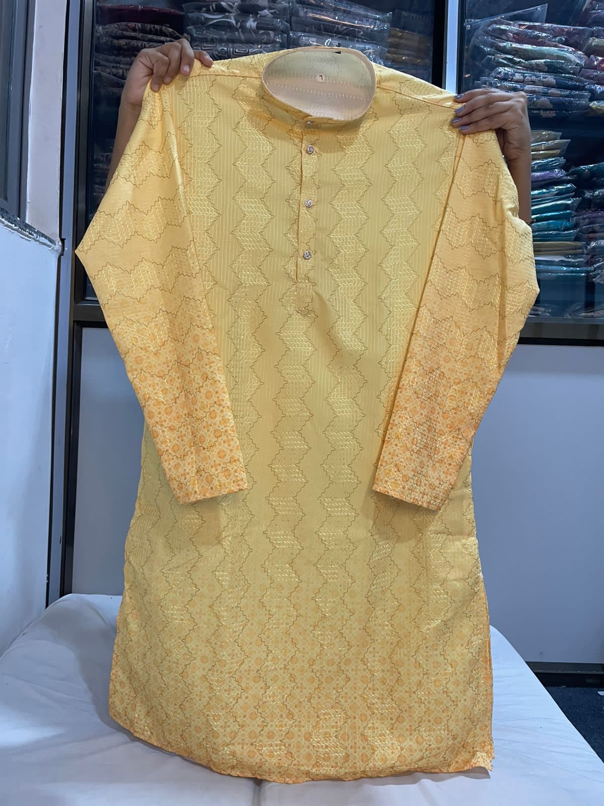 Yellow kurta with intricate patterns held up against a blurred background