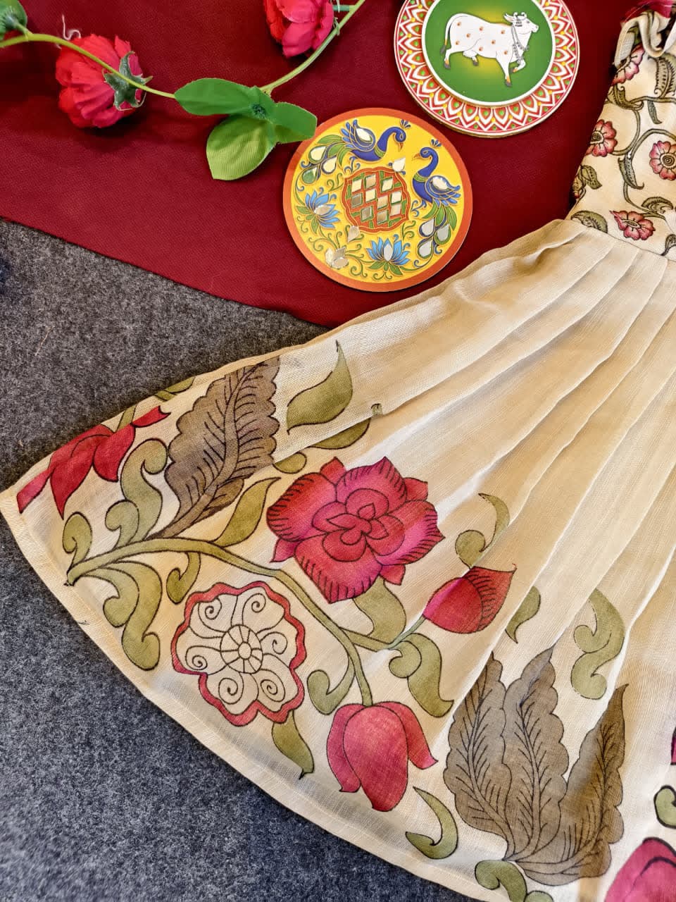Beige fabric with floral embroidery on a textured surface with decorative plates and flowers.