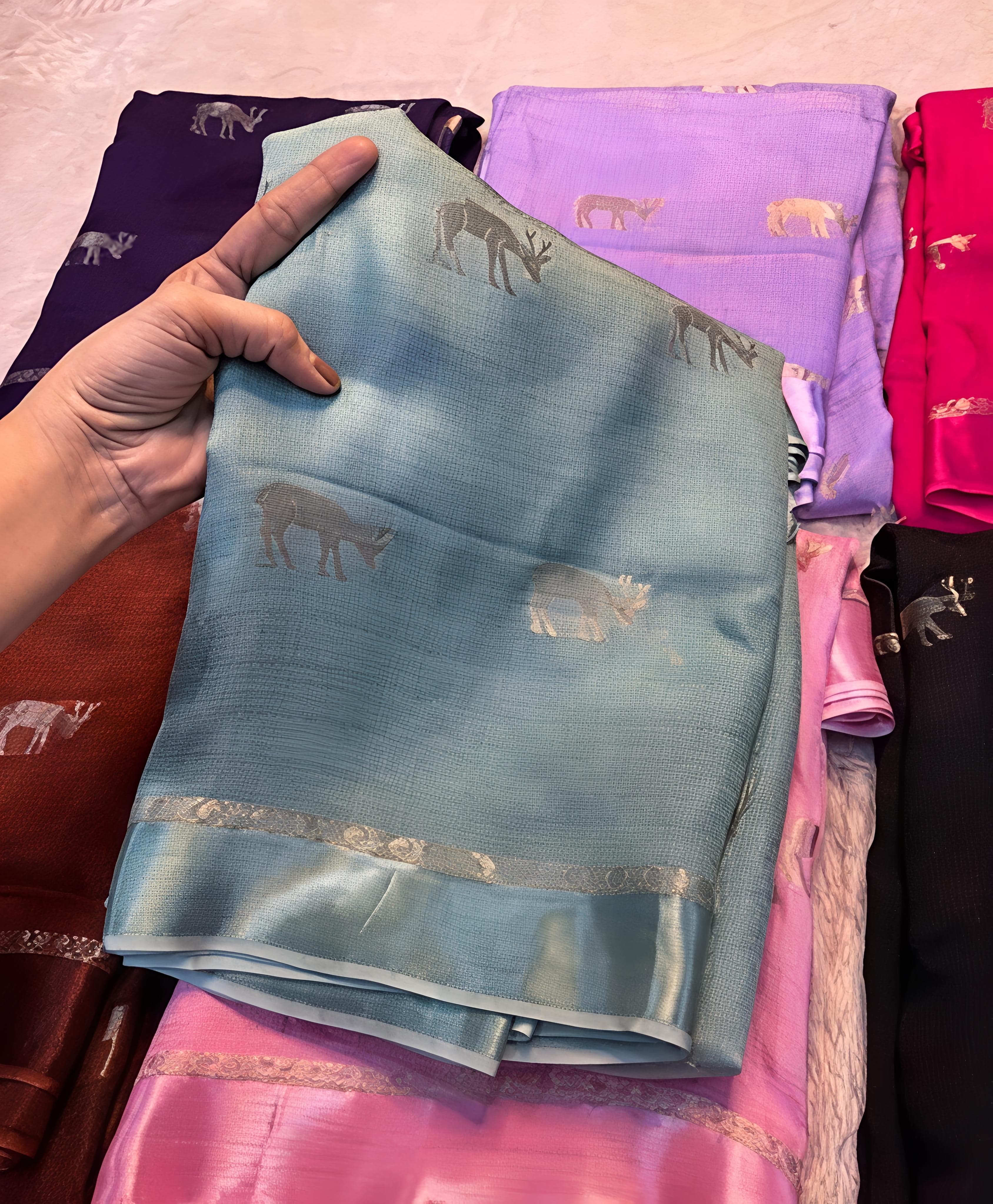 Light blue saree with elephant patterns against a background of other colorful sarees.